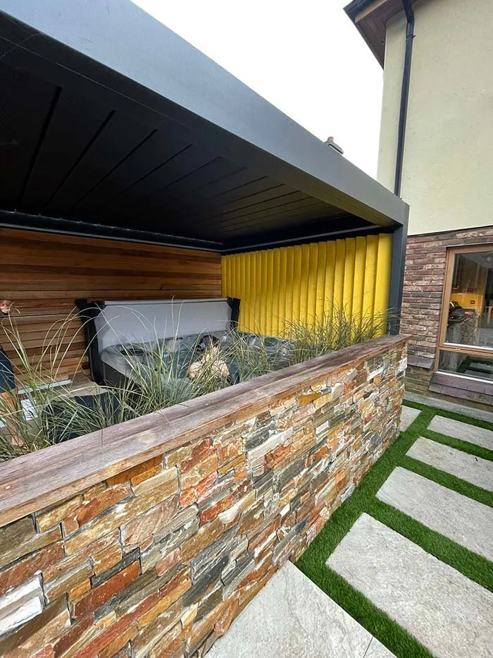 Wooden fence with alternating light and dark vertical slats, partial patio with stone steps, and a gray outdoor lounge chair.