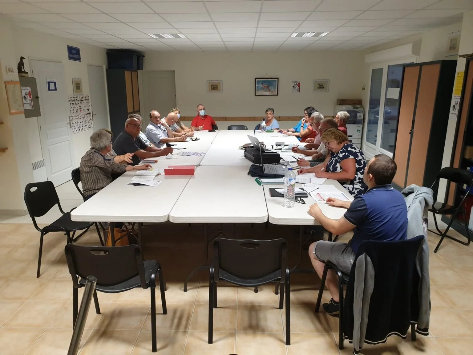 Groupe de personnes tenant une réunion dans une salle de conférence avec une grande table en forme de U, des documents, un ordinateur portable et des bouteilles d'eau