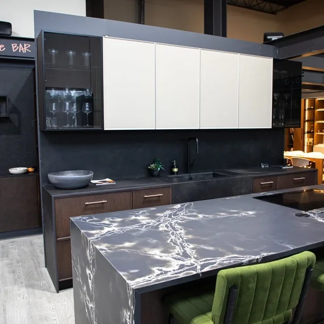 Modern kitchen with dark lower cabinets, light upper cabinets, marble island, black backsplash, and green chairs.