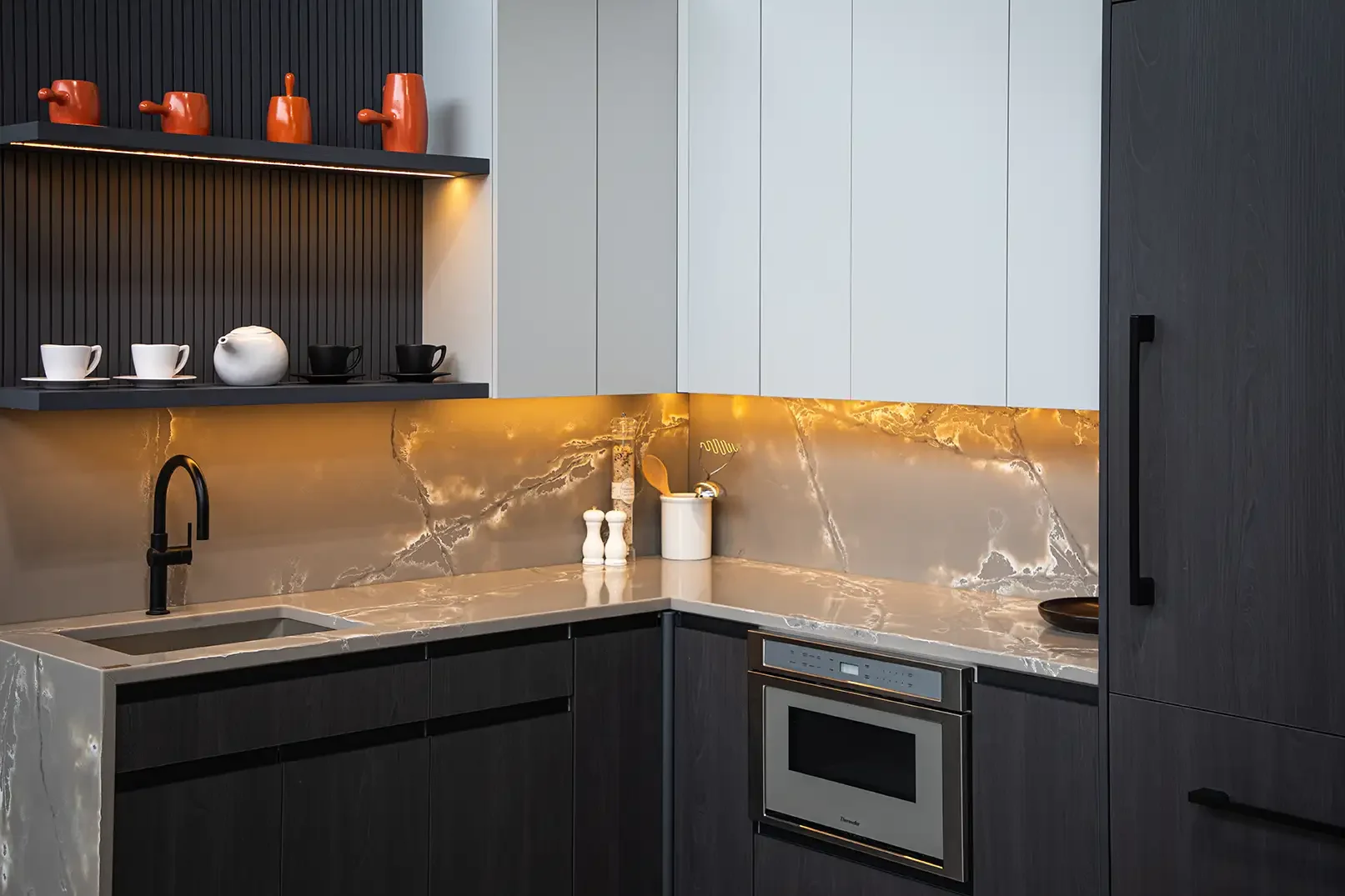 Modern kitchen with a marble countertop and backsplash, black and white cabinetry, open shelf with teapots and cups, and a built-in microwave.