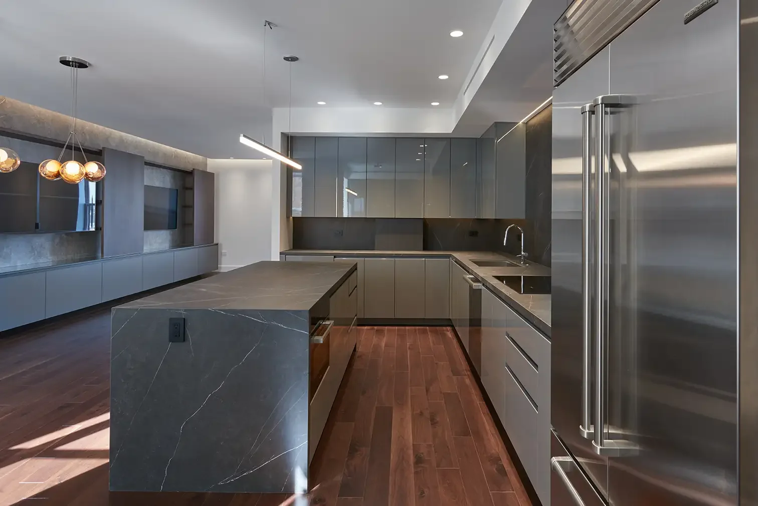 Modern kitchen with dark gray cabinets, stainless steel appliances, a marble island, and dark hardwood flooring.