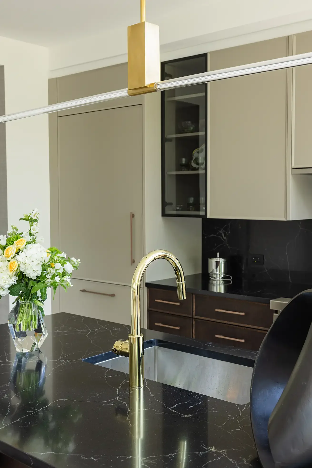 Modern kitchen with beige cabinets, black marble countertops, gold faucet, and a bouquet of white and yellow flowers in a glass vase on the counter.