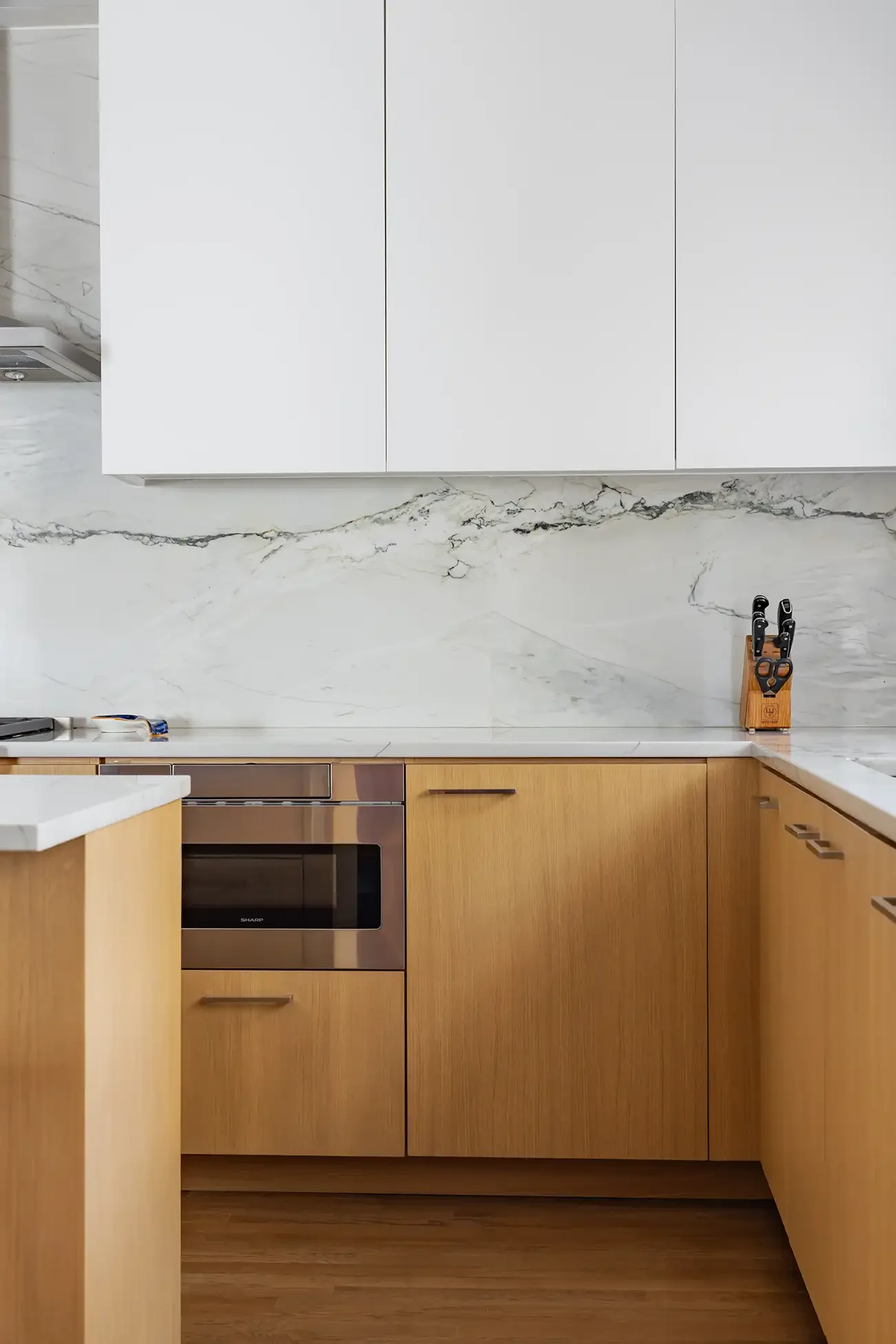 Modern kitchen with wooden cabinets, a stainless steel oven, a white marble countertop with gray veining, and a backsplash to match.