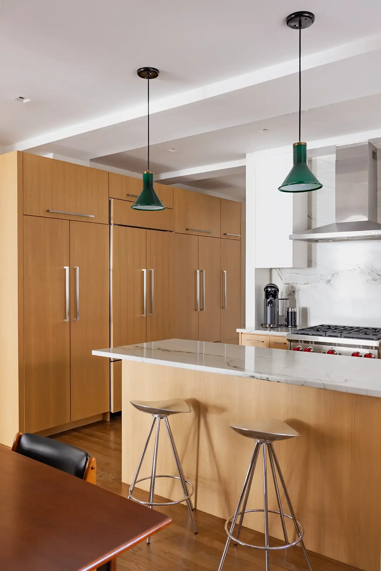Modern kitchen with wooden cabinets, a white marble countertop on an island, green pendant lights, and a stainless steel stove.