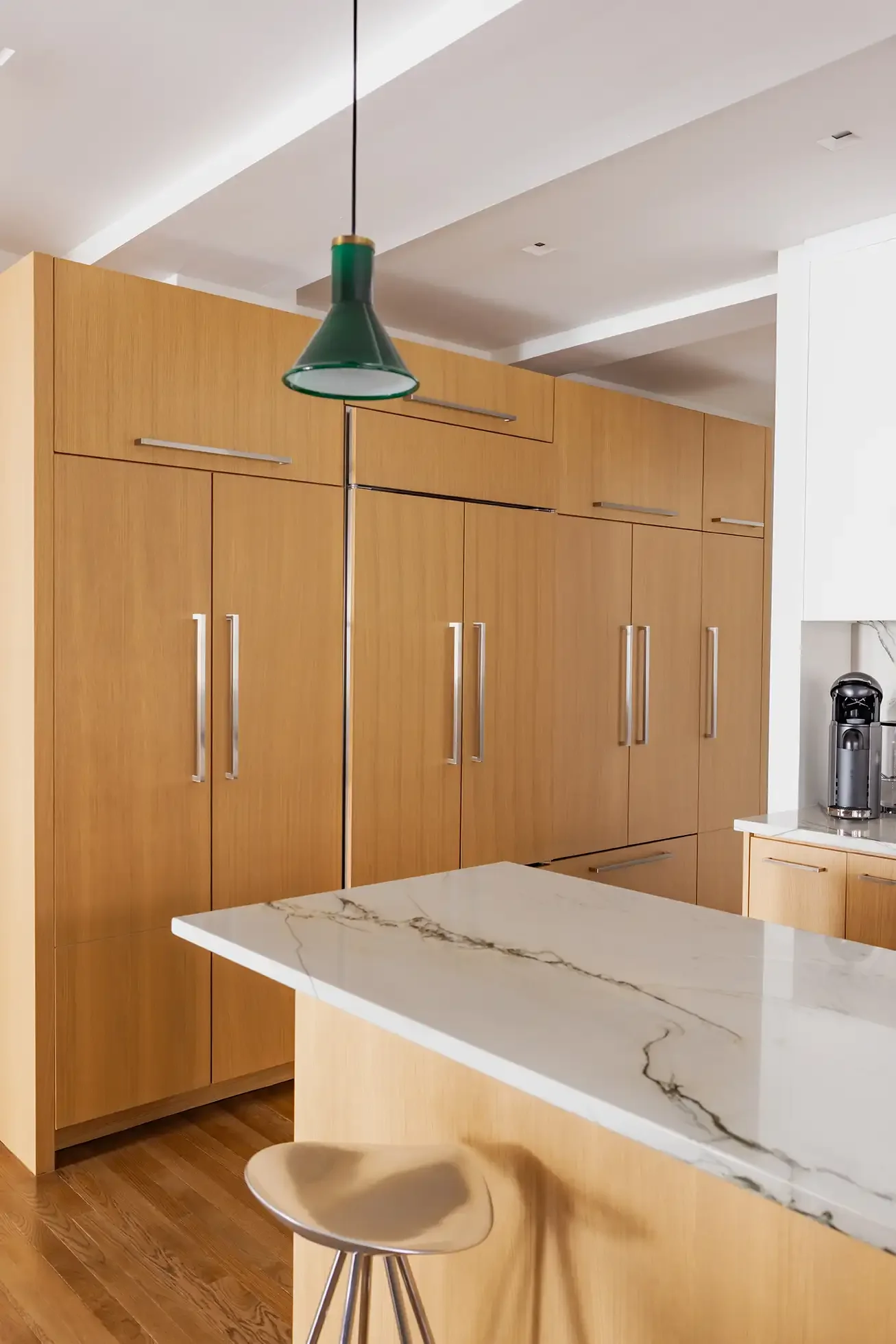 A modern kitchen with wooden cabinets, a marble countertop island, and a green pendant light hanging from the ceiling.
