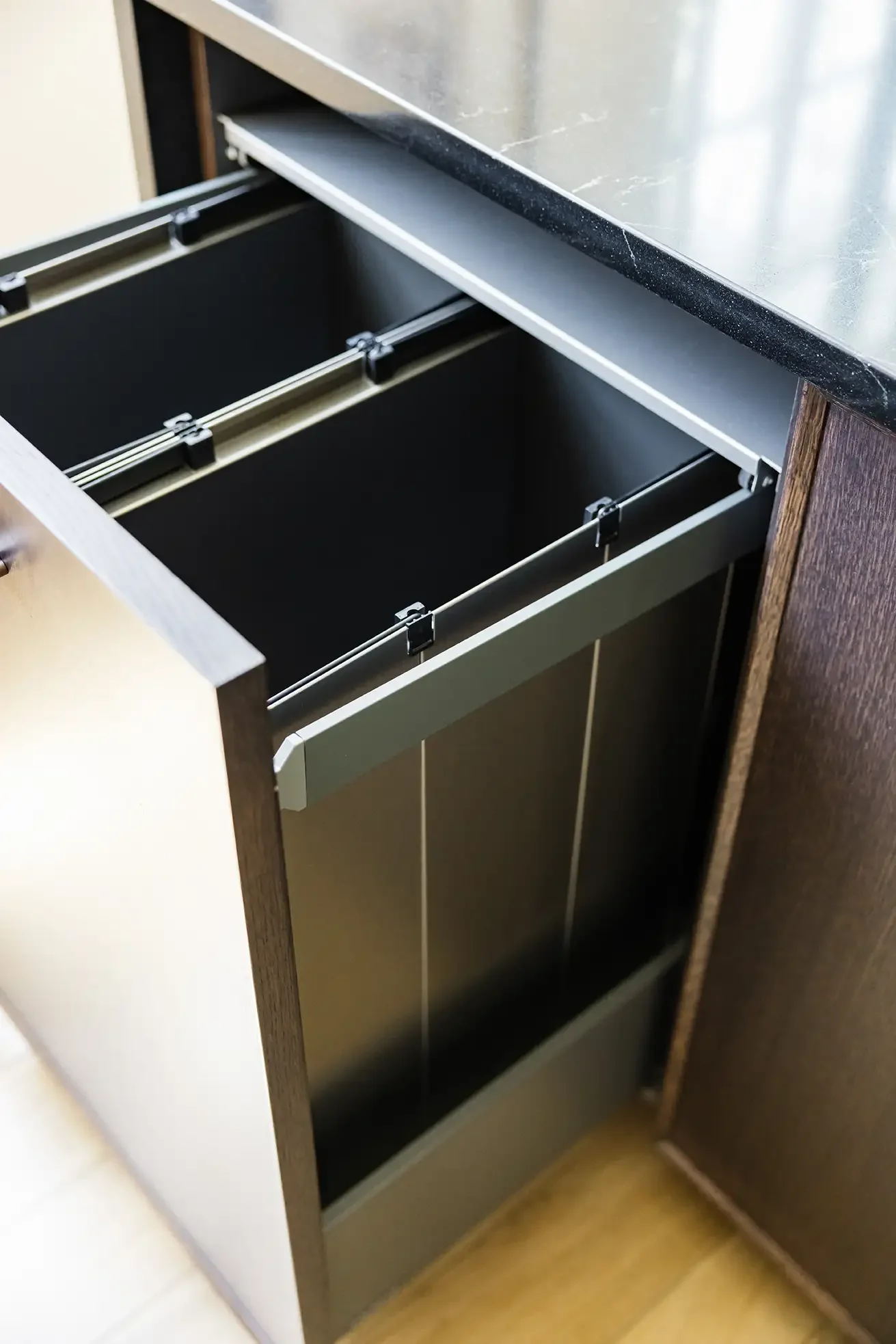 Open empty kitchen drawer with metal rails and black interior, part of dark wood cabinet with black marble countertop