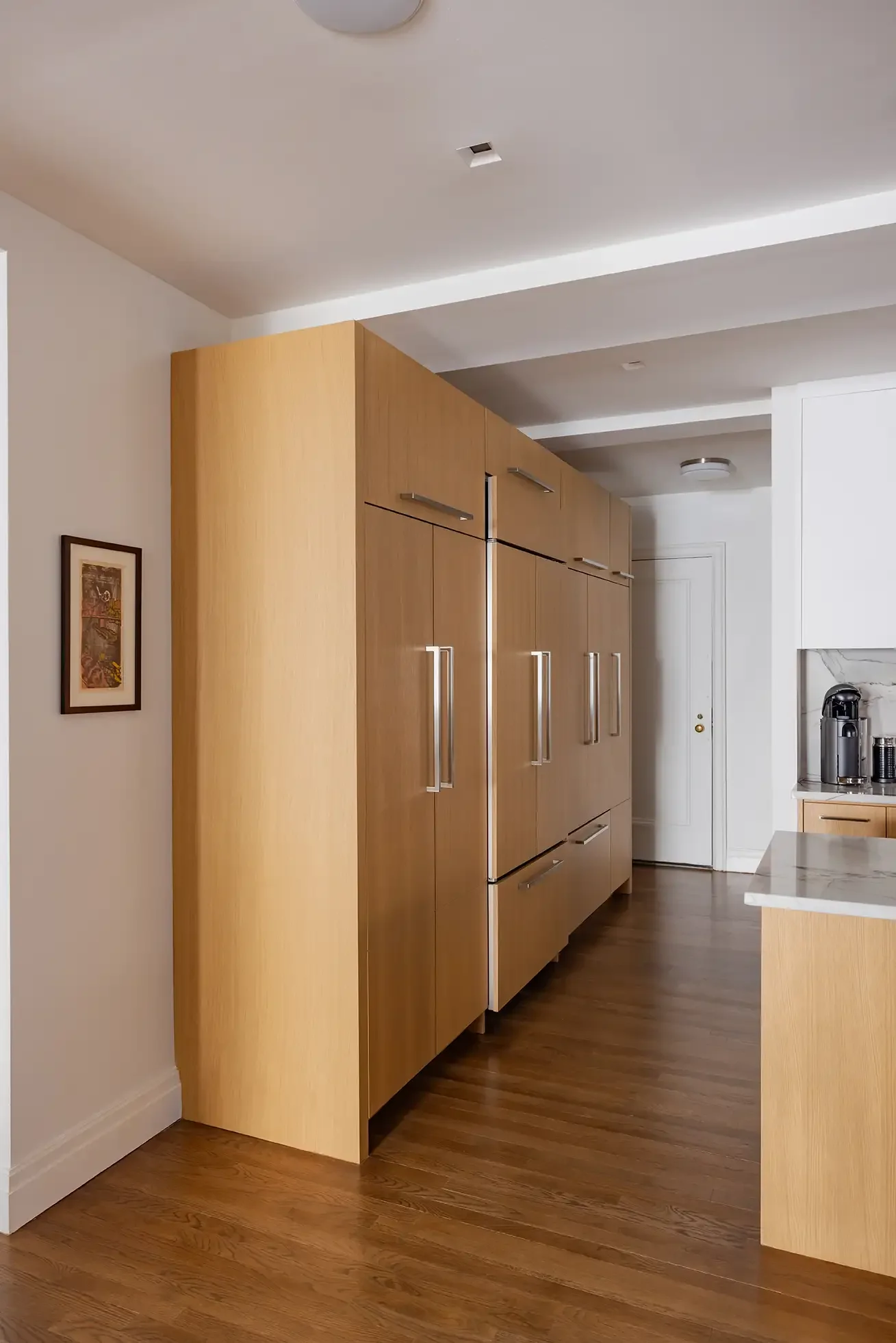 Modern kitchen with wooden cabinetry, hardwood floors, and a marble countertop with a coffee machine.
