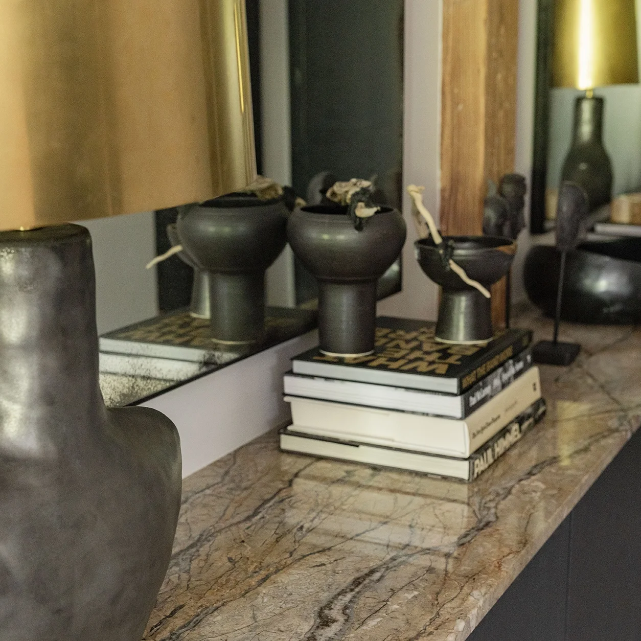 Decorative black bowls with white ties on top, placed on a small stack of books, on a marble countertop, with a mirror and various decorative objects reflected behind them.