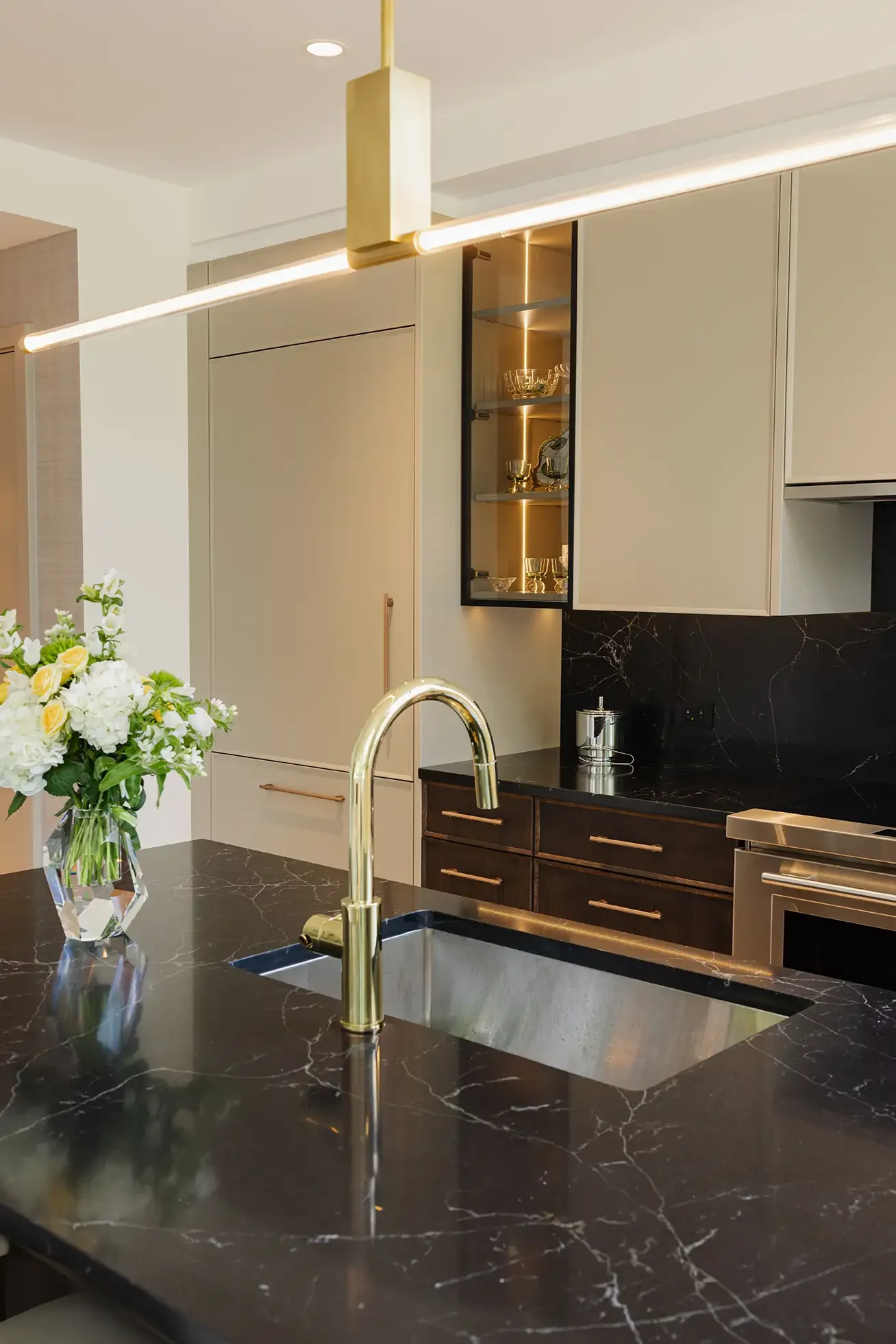 Modern kitchen with black marble countertops, gold faucet, white cabinets, and a black glass display cabinet with glassware.