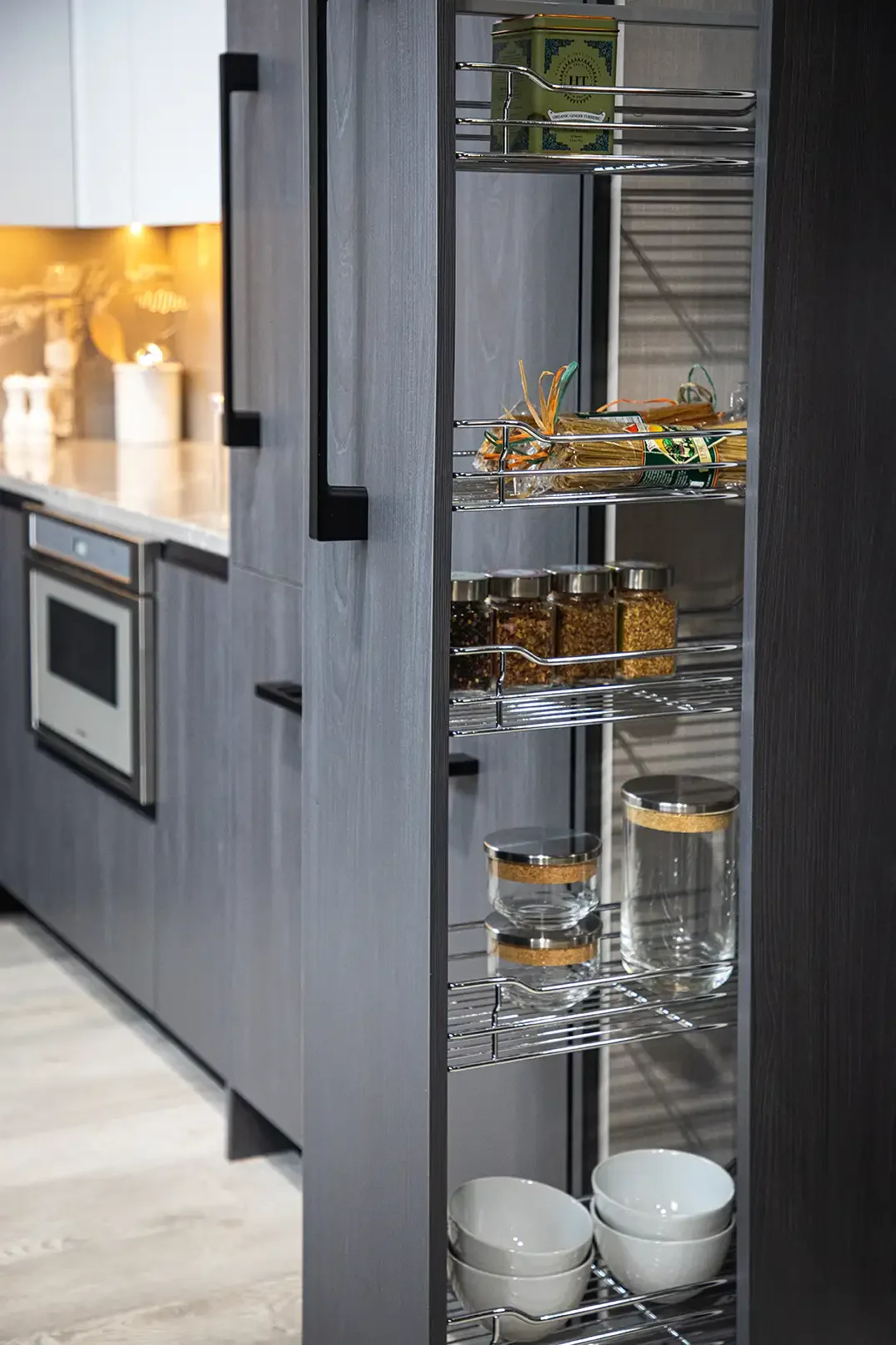 Open kitchen cabinet with wire shelves containing spice jars, bowls, and other kitchen items.
