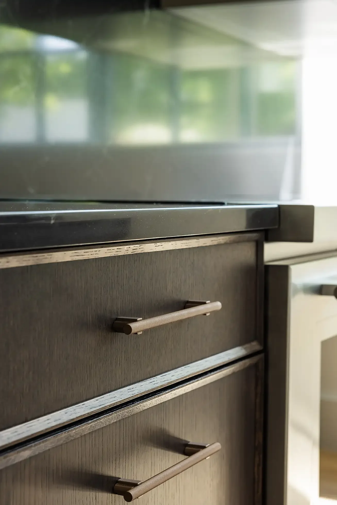 Close-up of a wooden cabinet with metal handles, next to a modern white appliance, with a window showing greenery in the background.