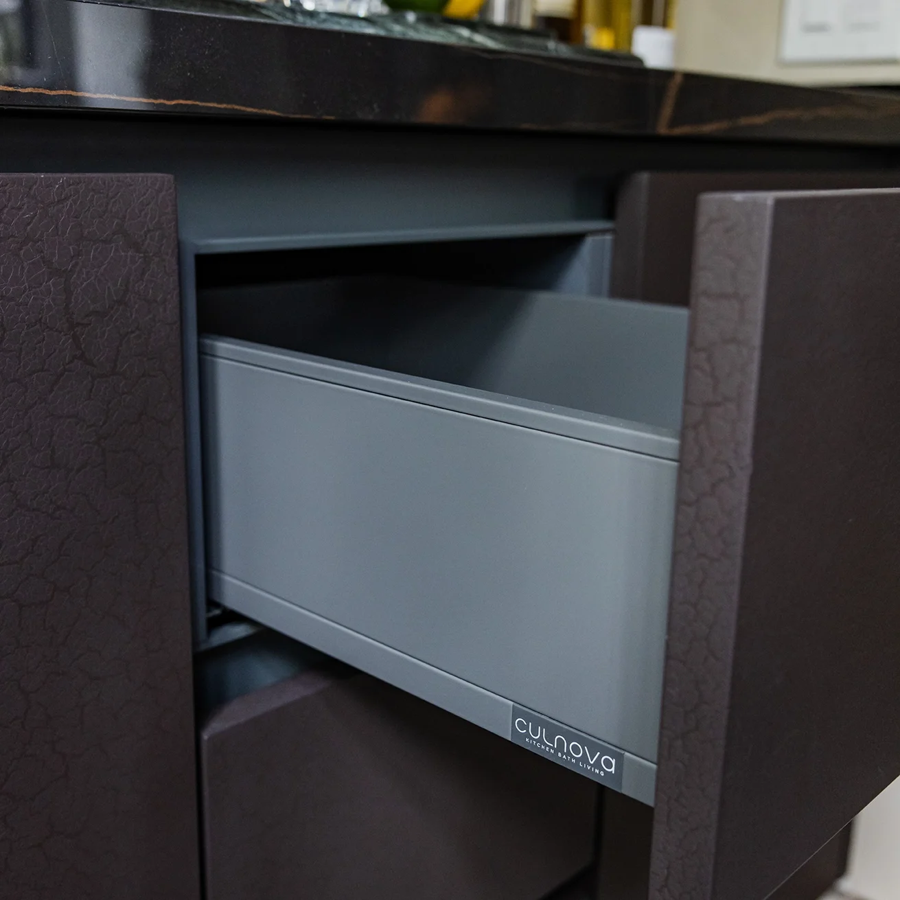 Close-up of an open grey drawer in a black cabinet, with a label that reads 'Culnova Kitchen Bath Living'.