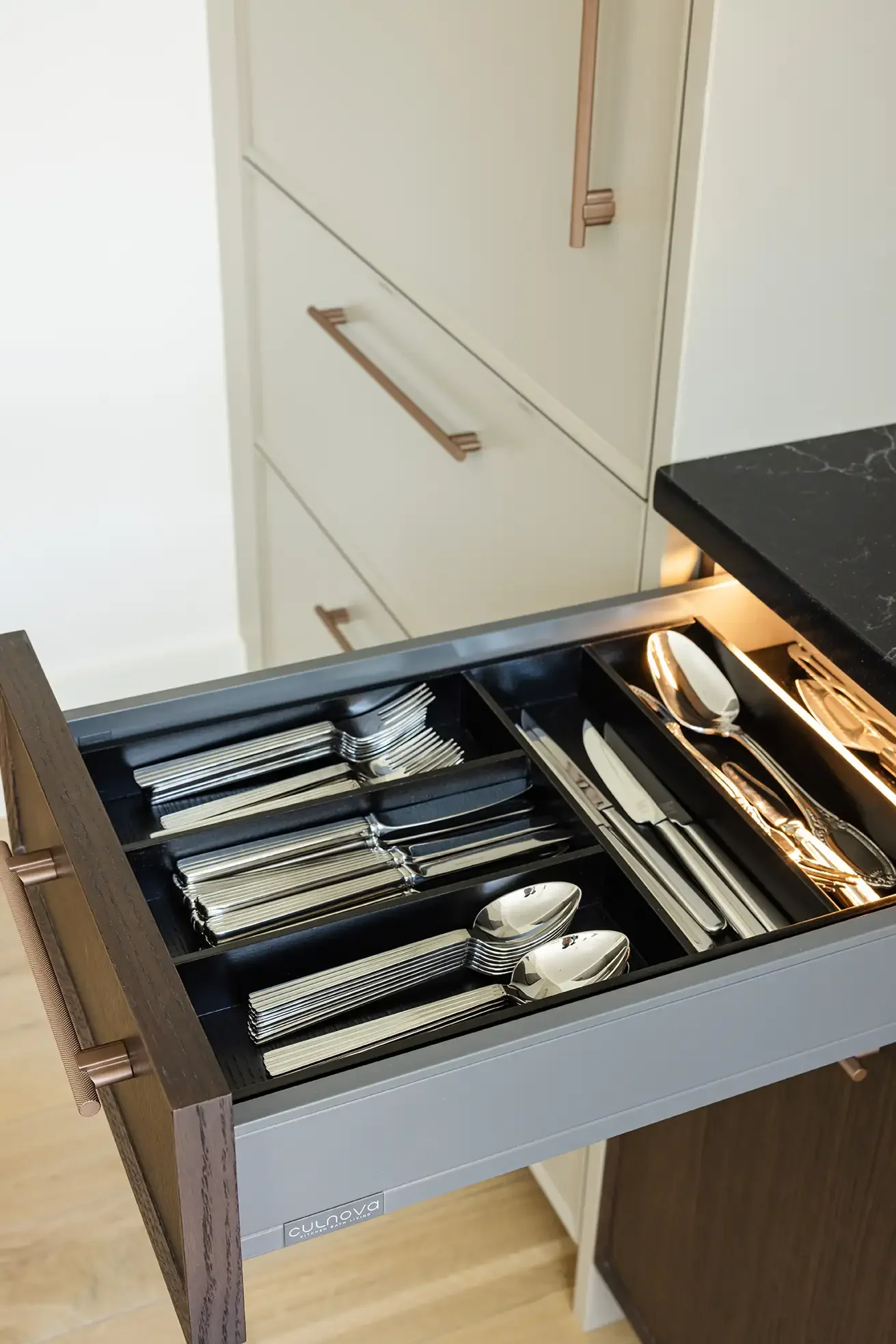 Open kitchen drawer containing stainless steel utensils including spoons, forks, and knives, organized in separate compartments.
