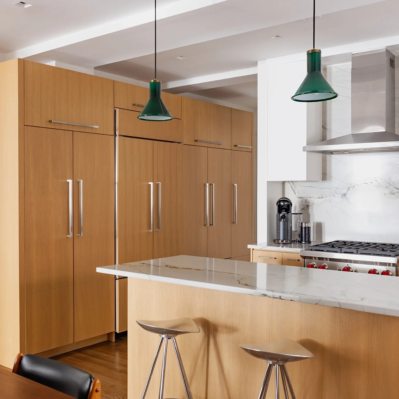 Modern kitchen with wooden cabinets, a marble countertop, two green pendant lights, and stainless steel appliances including a range hood and a coffee machine.