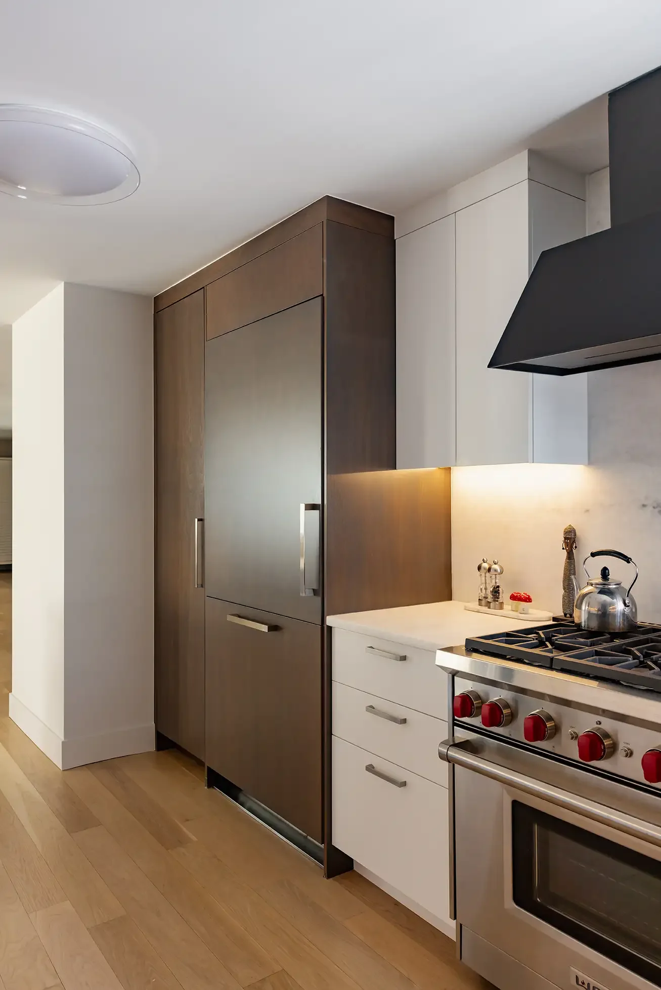Modern kitchen with dark and white cabinets, stainless steel stove with red knobs, and wooden flooring.