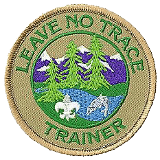 A circular embroidered patch with the words 'Leave No Trace' and 'Trainer' around the border, featuring a landscape with trees, mountains, a stream, and wildlife.