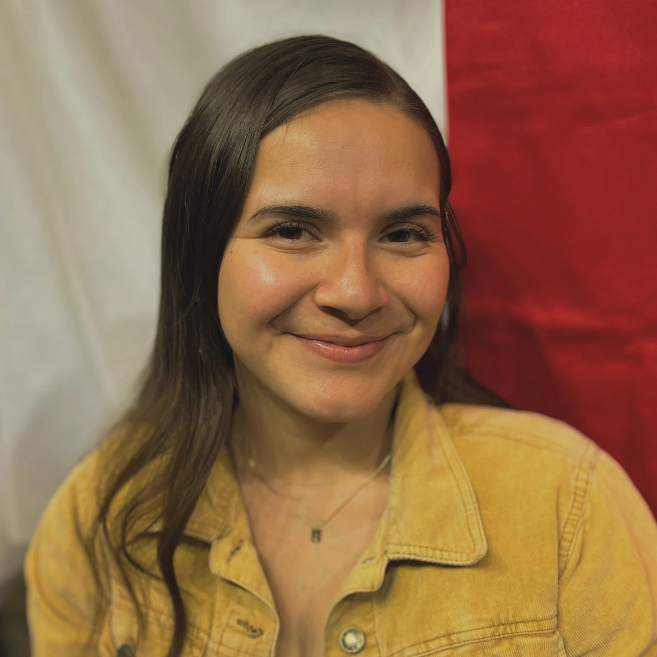 A smiling man dressed in white clergy robes with a green stole, sit