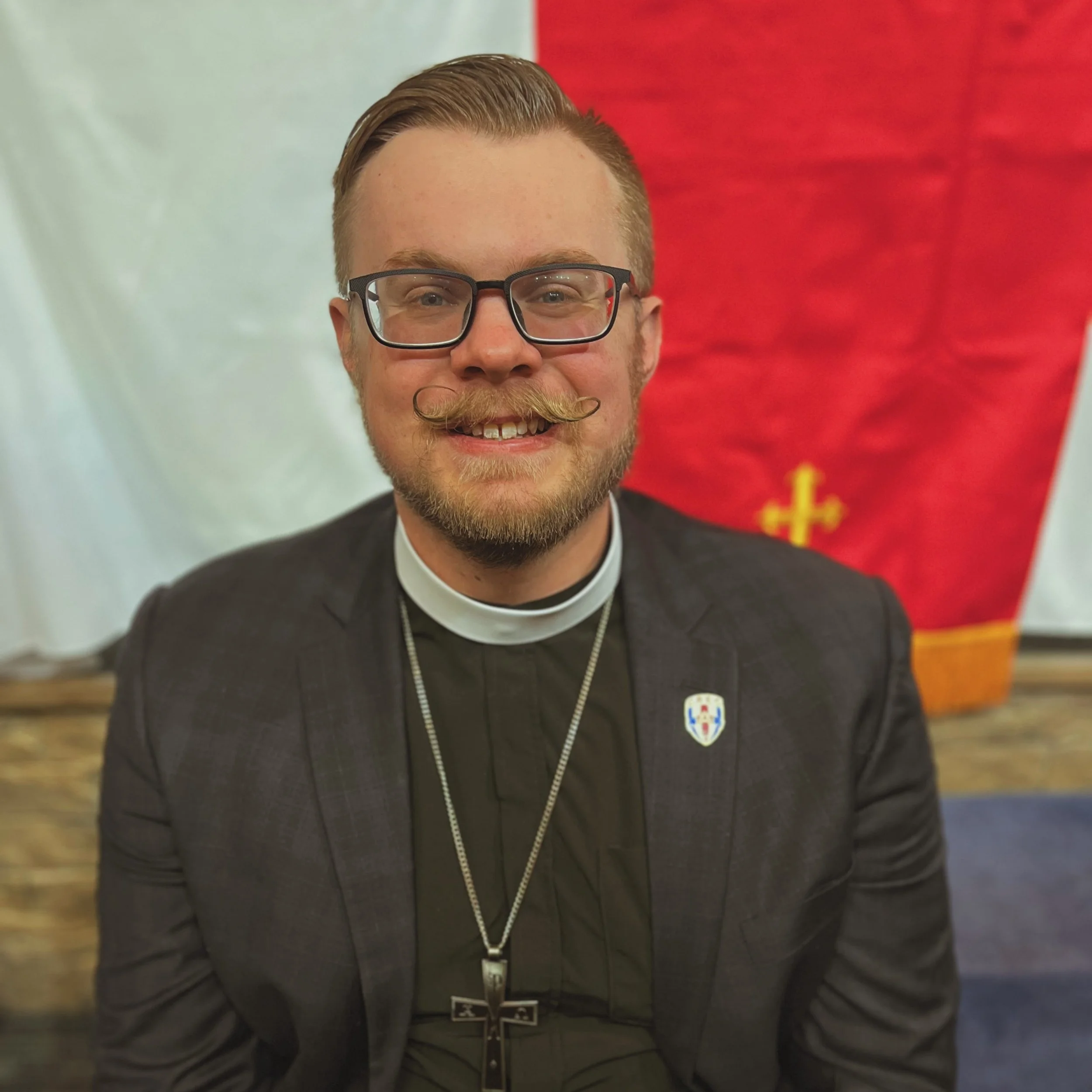 A gold shield emblem with a crown on top, featuring a gold cross in the center.