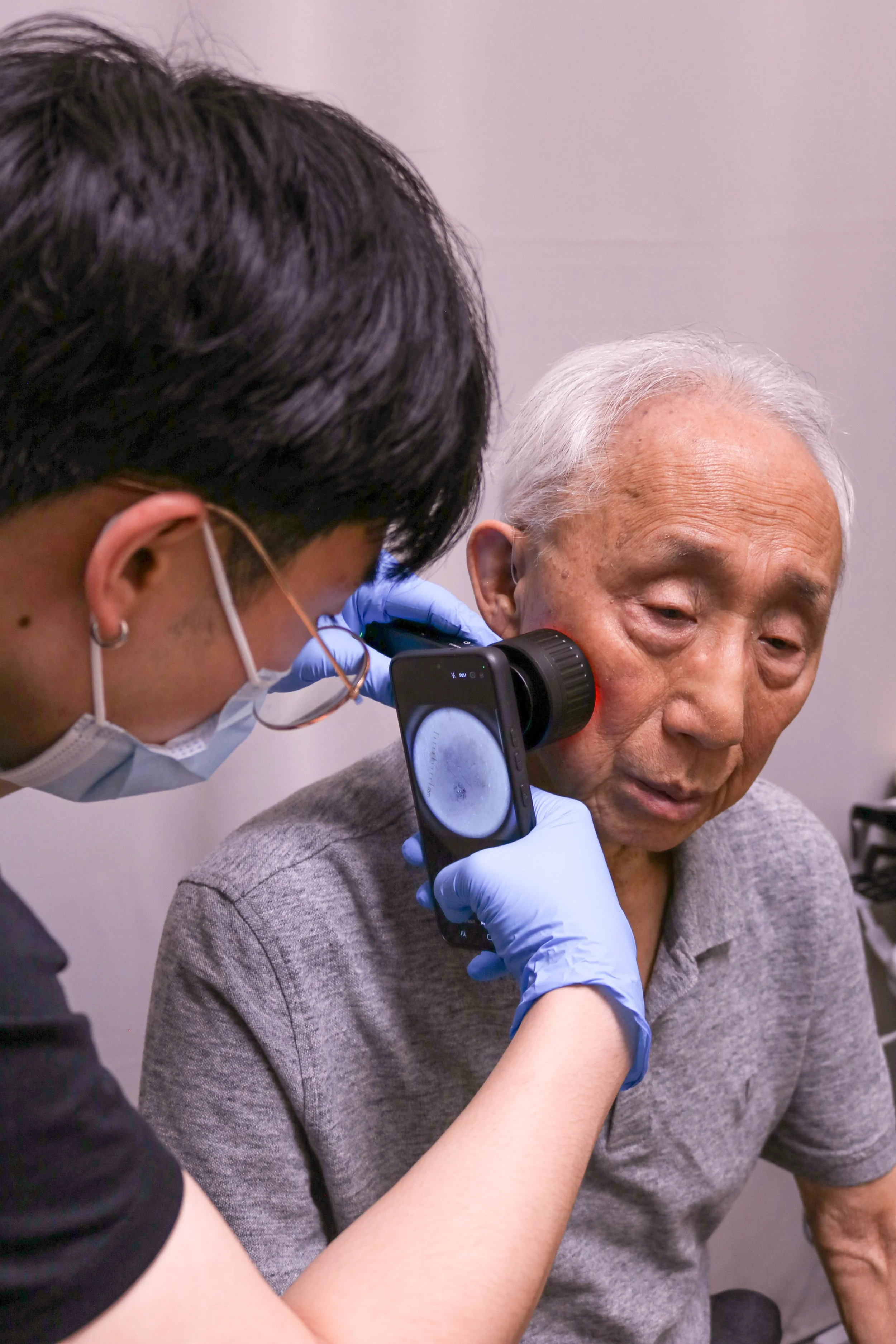 A healthcare worker examining an elderly man's lesion with an dermatoscope.