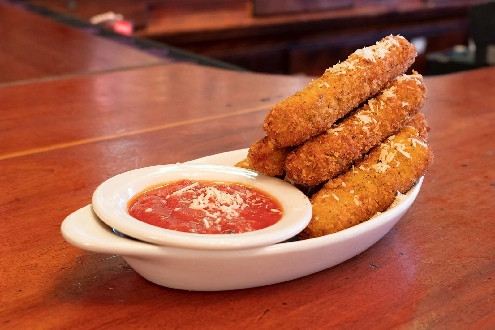 Breaded cheese sticks on white plate with red marinara sauce