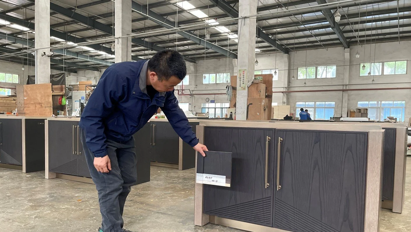 A man in a blue jacket examining a black and gray cabinet inside a woodworking workshop