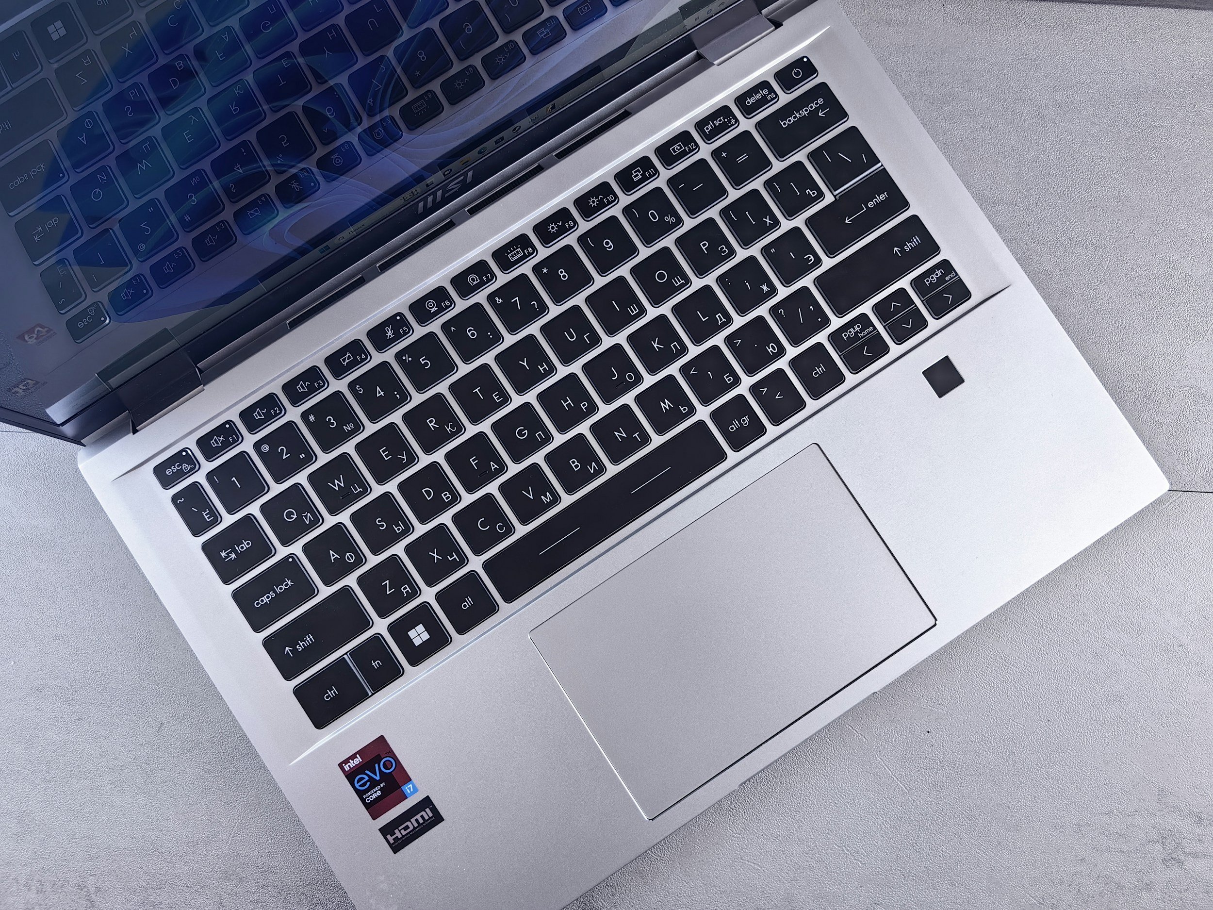 Top view of a silver laptop keyboard and trackpad on a light-colored surface.