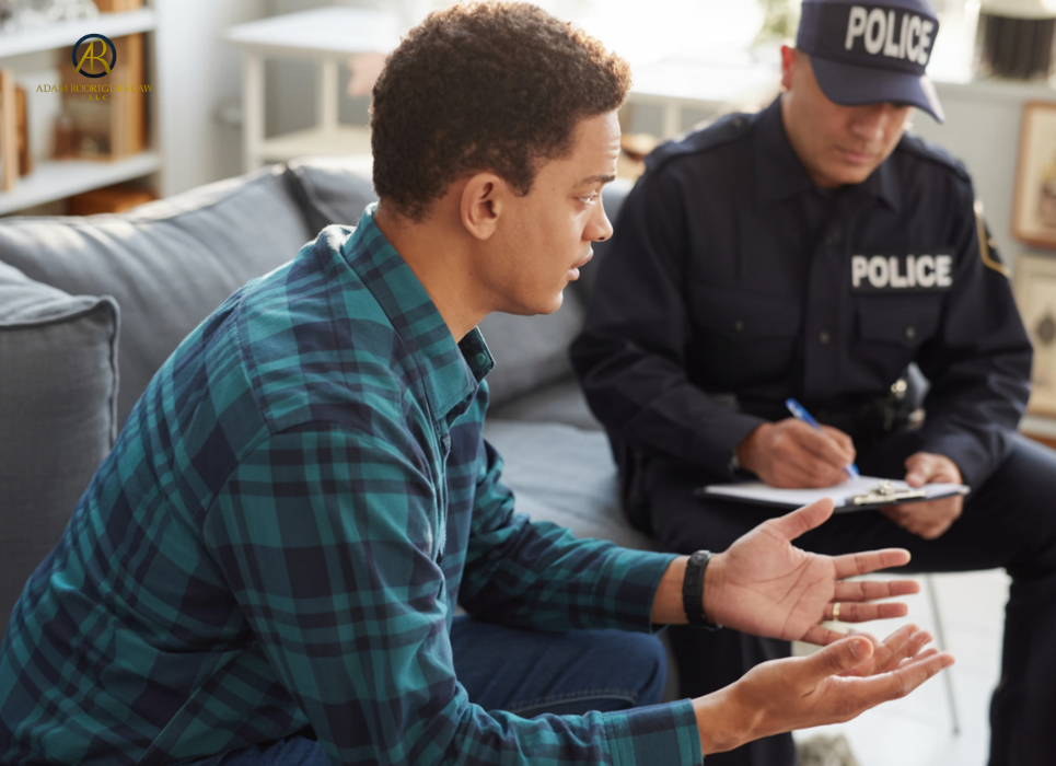 Police officer interviewing a witness during a criminal investigation while taking notes on a clipboard. Adam Rodrigues Law logo in the top left hand corner