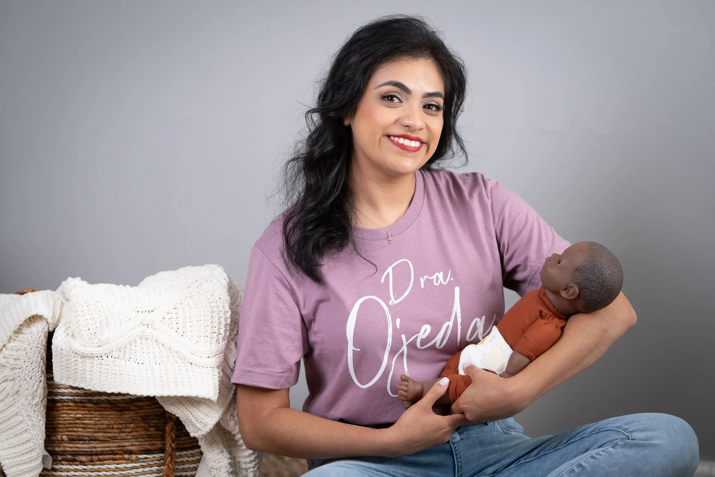 A smiling woman with dark hair, cradling an African baby doll.