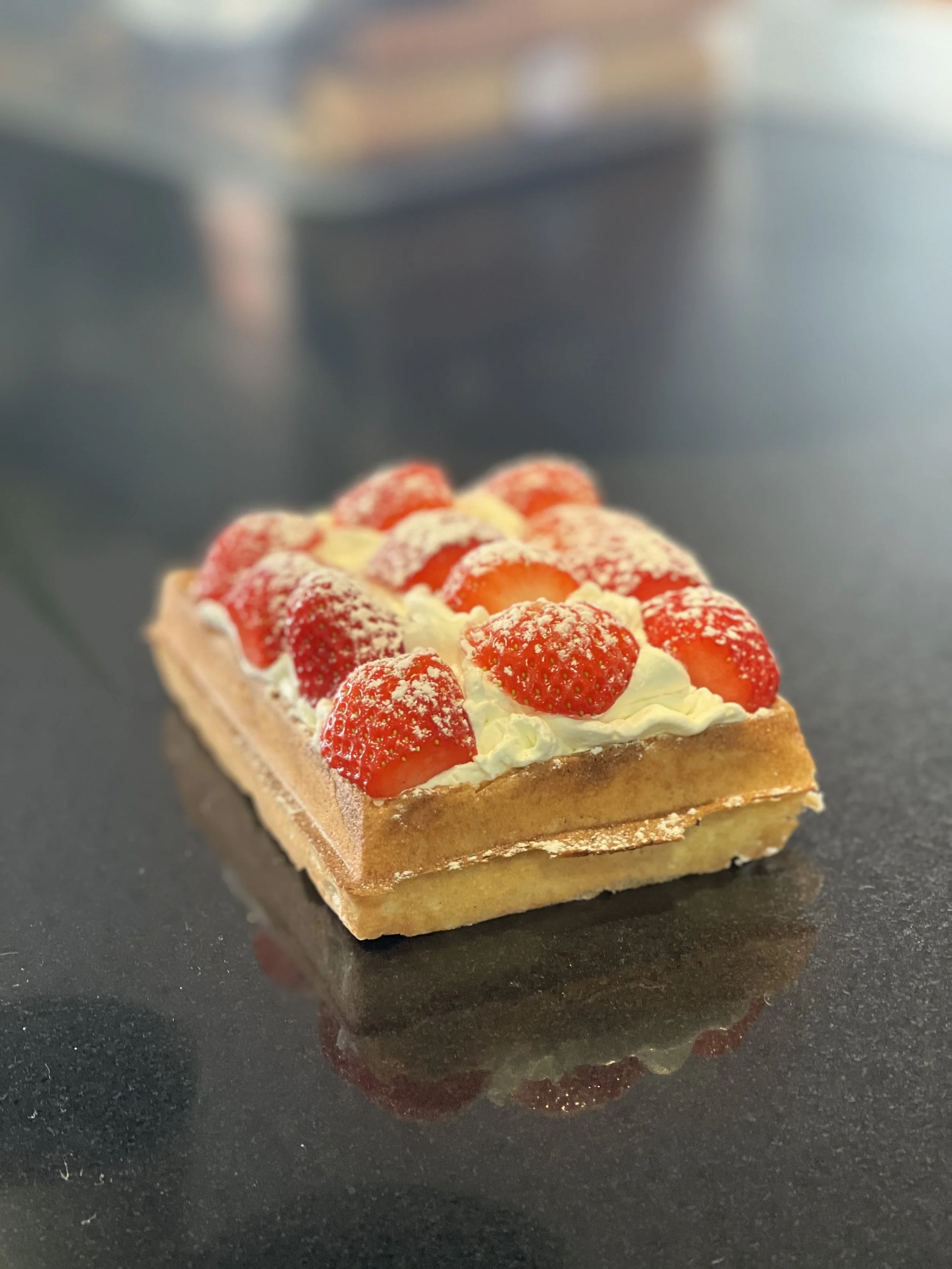 Gâteau rectangulaire avec des fraises fraîches et de la crème à la surface, posé sur une surface noire.