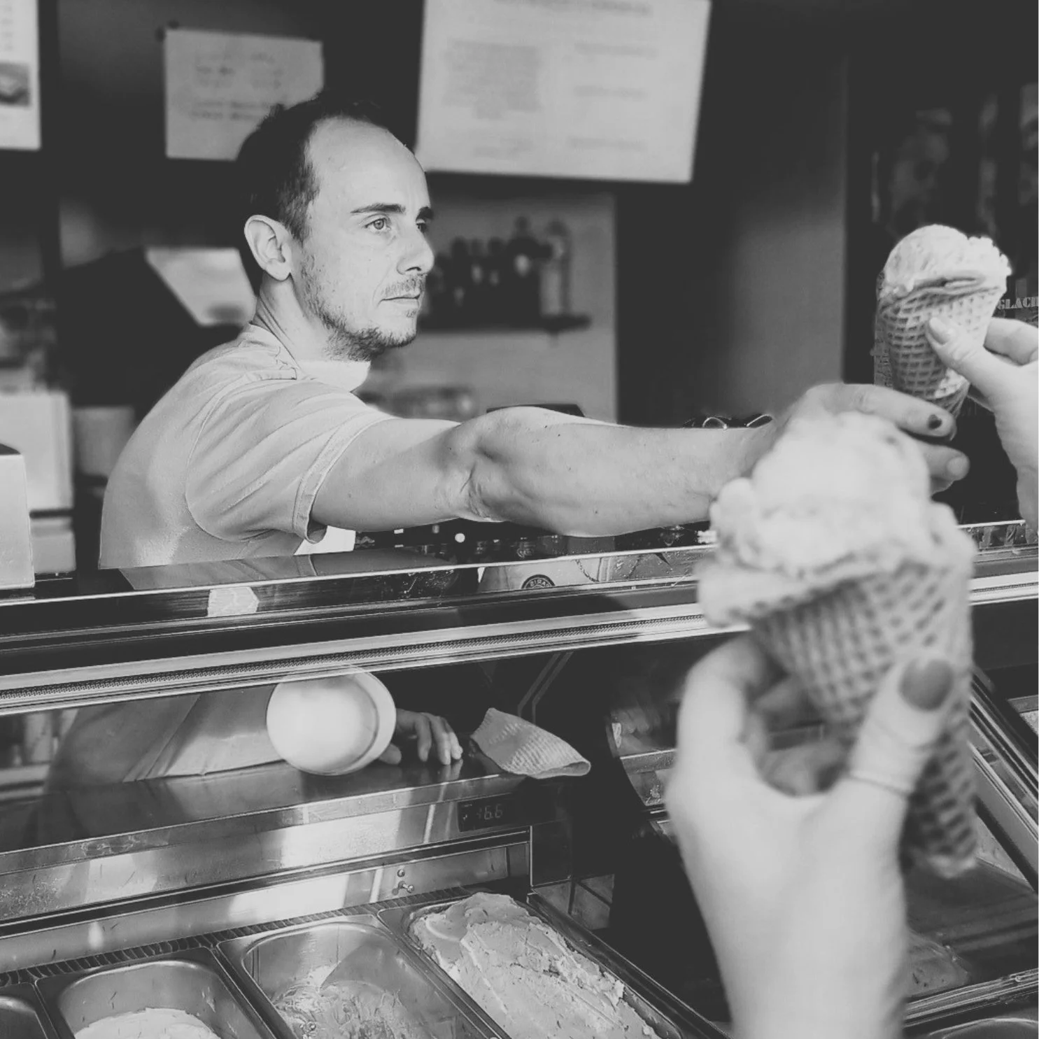 Un serveur sert des glaces en cornet à des clients dans une vitrine de glacier.