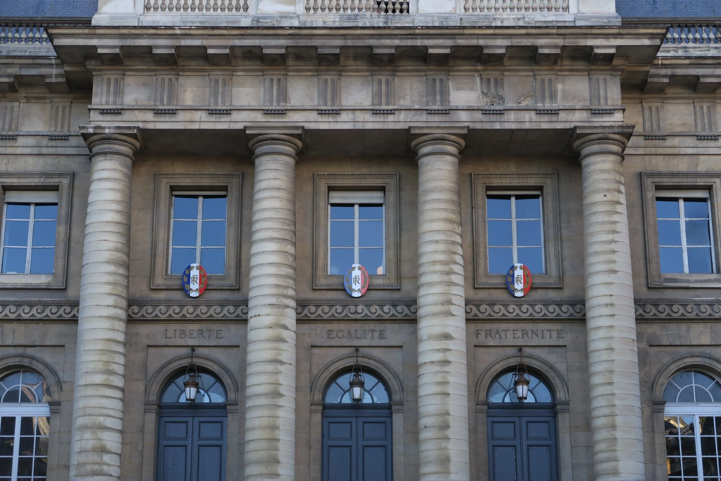 Façade de la Cour d'appel de Paris vec quatre colonnes, trois fenêtres au-dessus, des insignes français, et les mots 'Liberté, Égalité, Fraternité' inscrits en dessous des fenêtres.