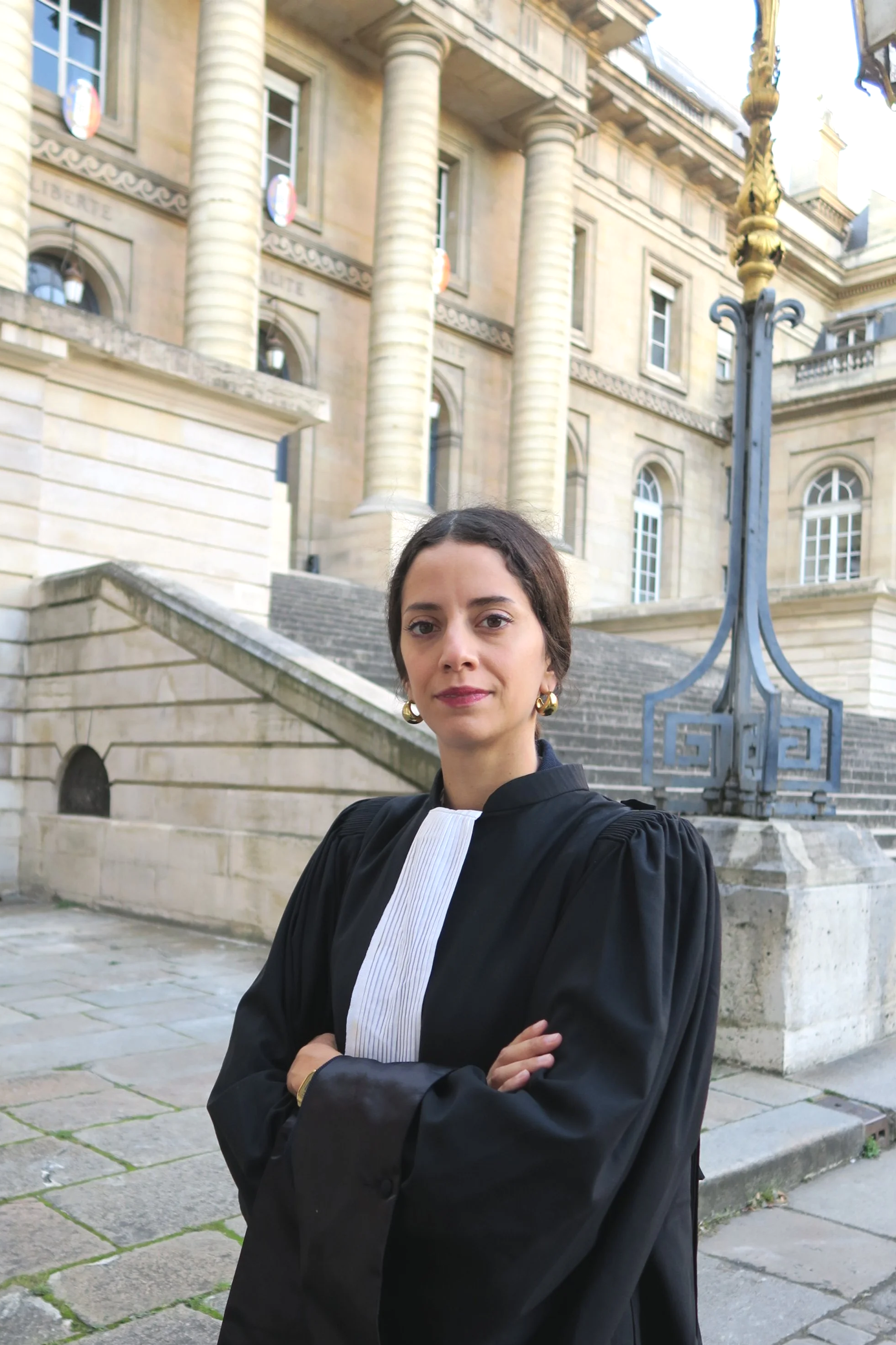 Une femme portant une robe d'avocat, avec  la Cour d'Appel de Paris en arrière-plan