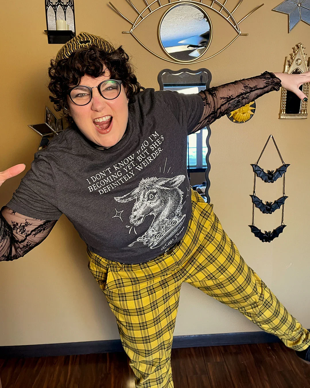 Dean Rodriguez shows off an outfit from their Letter Shoppe store, leaning forward on one leg and spreading their arms, growling into the camera fiercely.