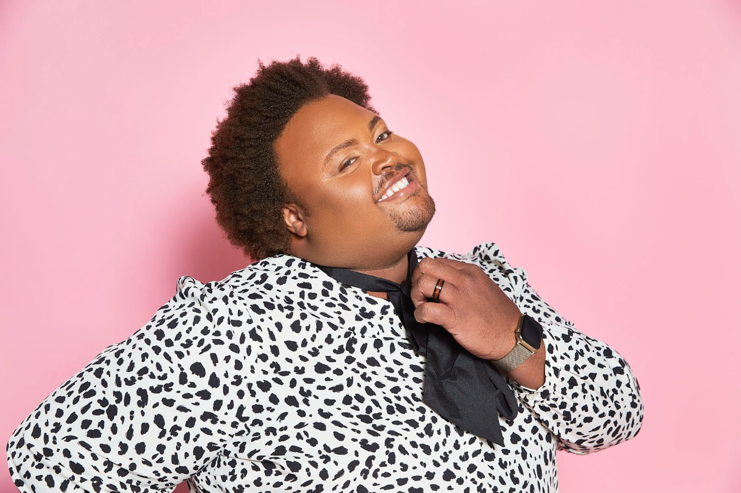 Dr. Jonathan P Higgins in a spotty black and white top with a black silky scarf around their neck, head tilted back and smiling coyly at the camera. They wear a black and wood ring and a fancy smartwatch.