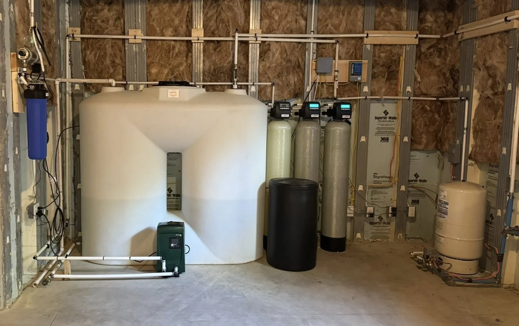 A water treatment or filtration system installed in a utility room, featuring large tanks, filters, and control panels.