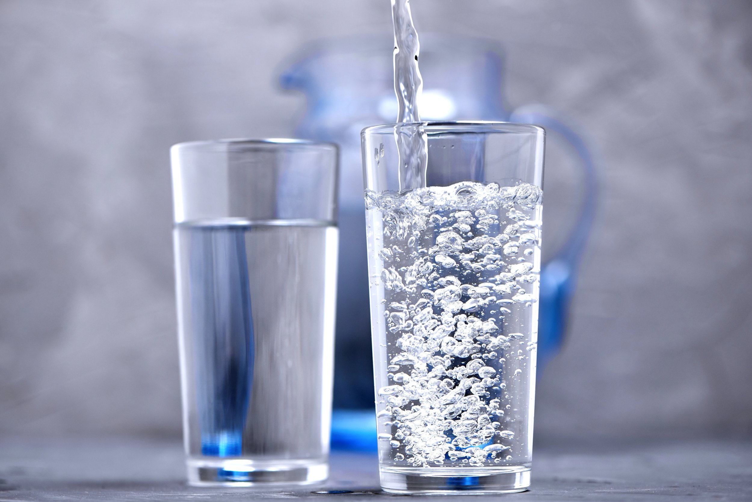 A close-up of a glass being filled with water from a pitcher, with another glass already filled in the background.