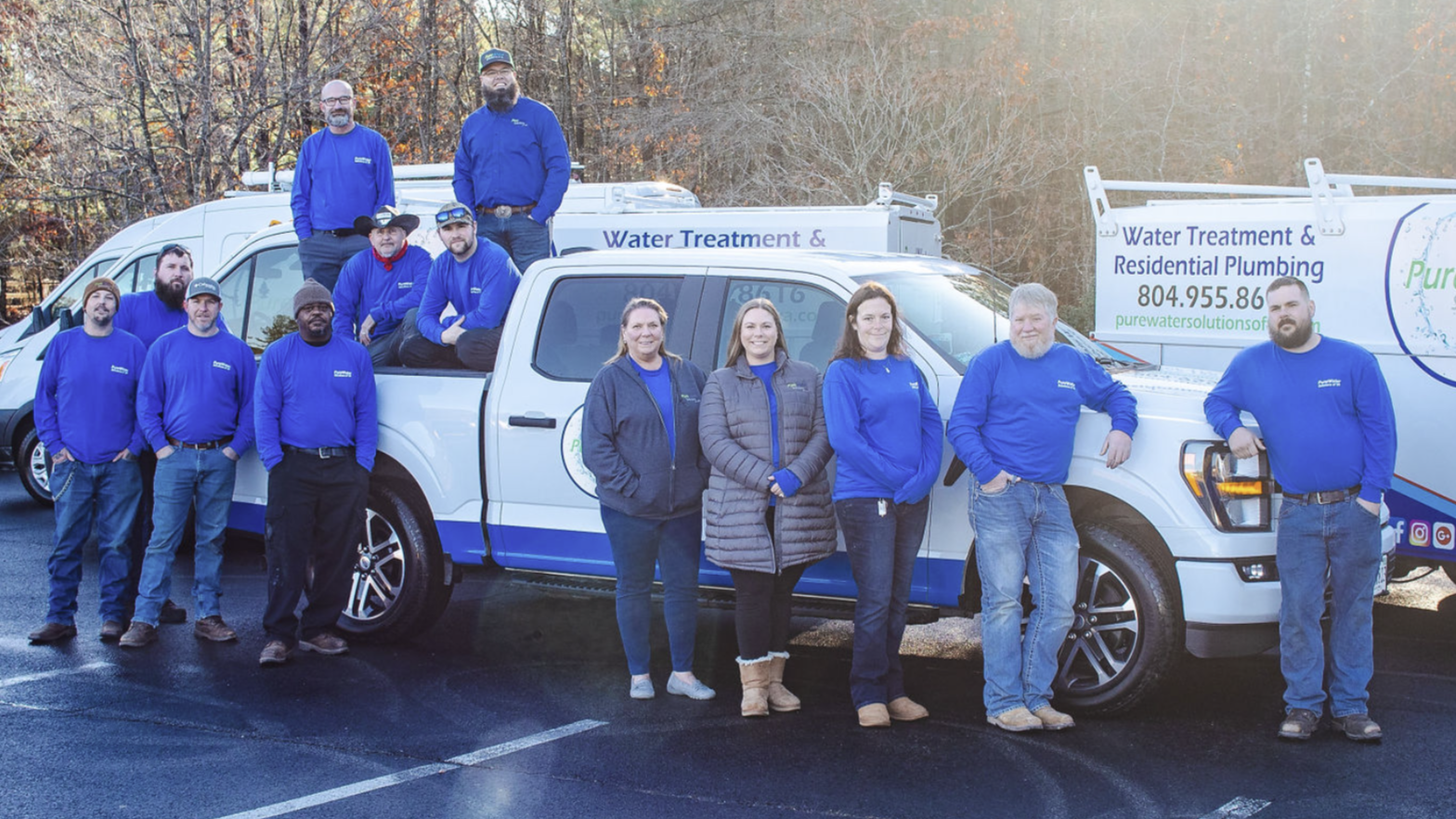 Group of water treatment and plumbing professionals standing in parking lot with service trucks displaying company branding.
