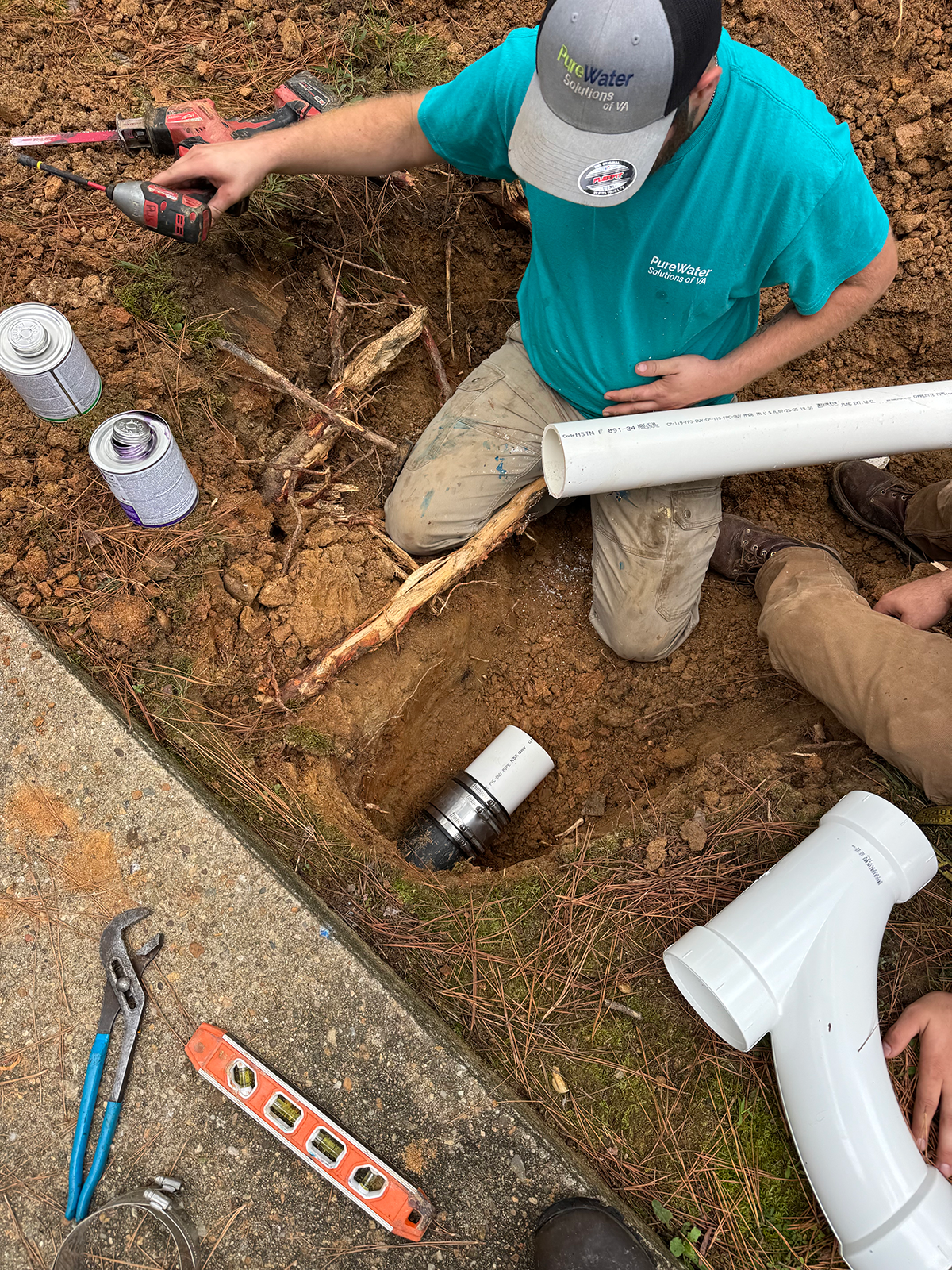 Worker installing underground water pipes in a trench, with tools and materials nearby, at a construction site.
