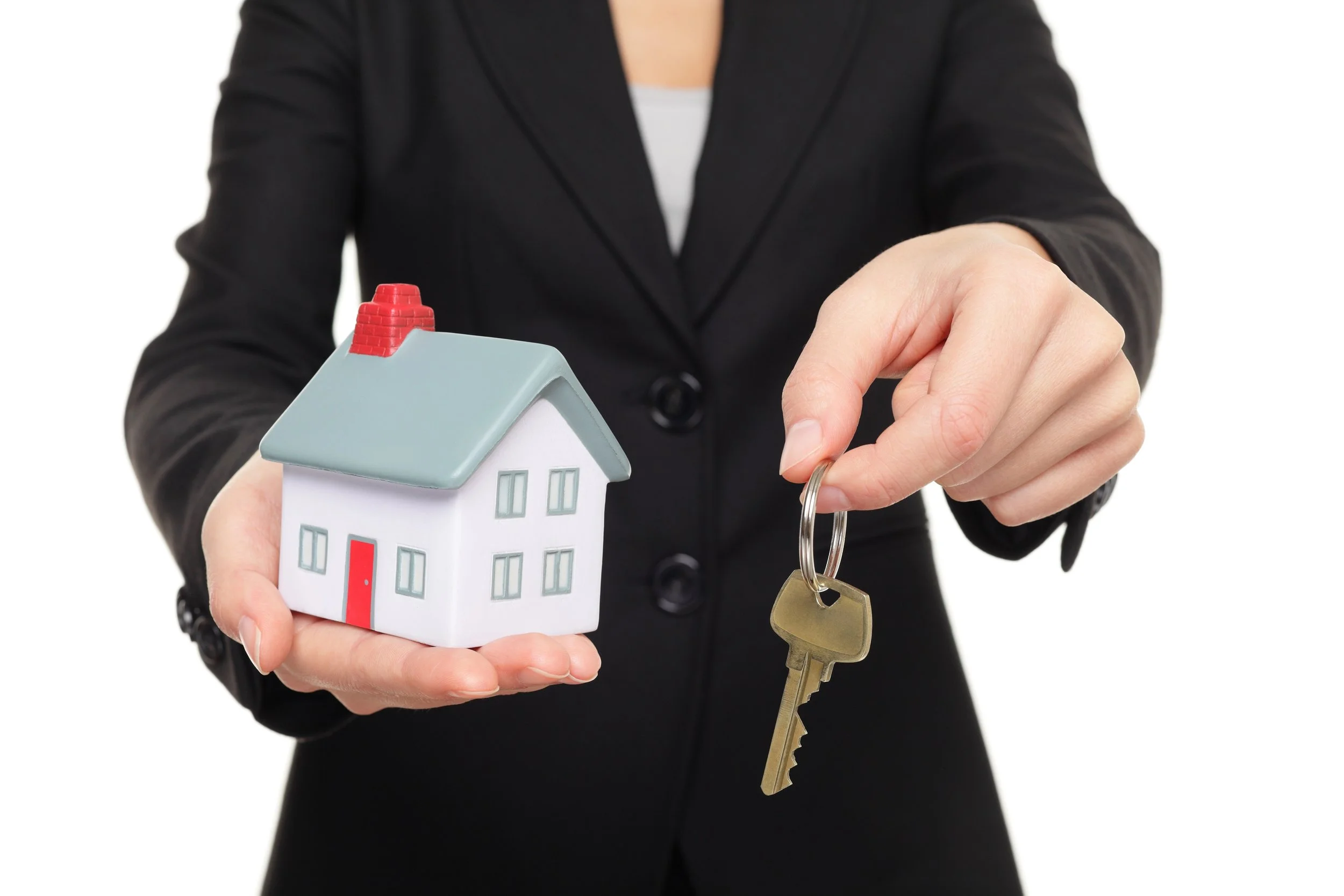 Person in black suit holding a small house model in one hand and a key with a keyring in the other.