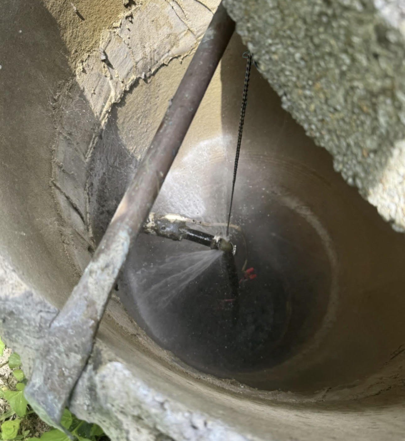 A well with a bucket and a water pump inside, water spraying from the pump into the bucket.