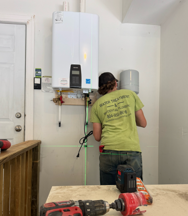 Technician in a green shirt installing or servicing a water heater in a utility room.