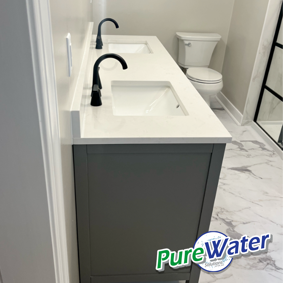 Modern bathroom with a white double sink vanity with black faucets, a toilet in the background, gray cabinetry, and marble floor tiles. There is a logo for Pure Water Solutions in the bottom right corner.