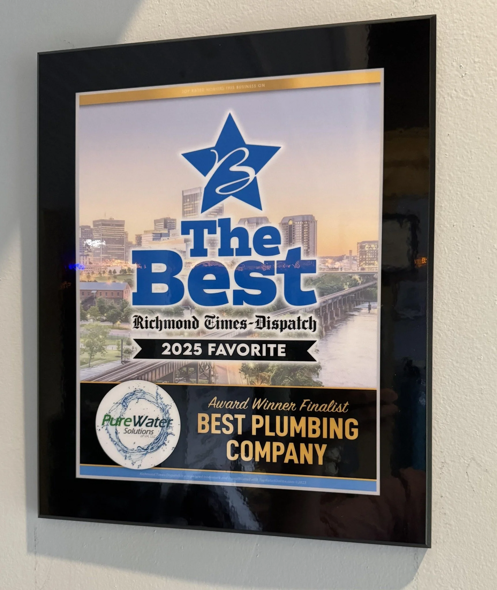 An award plaque with the text 'The Best Richmond Times-Dispatch 2025 Favorite Award Winner Finalist Best Plumbing Company.' The plaque features a blue star logo at the top, a city skyline with a river in the background, and a circular logo for Pure Water Solutions.