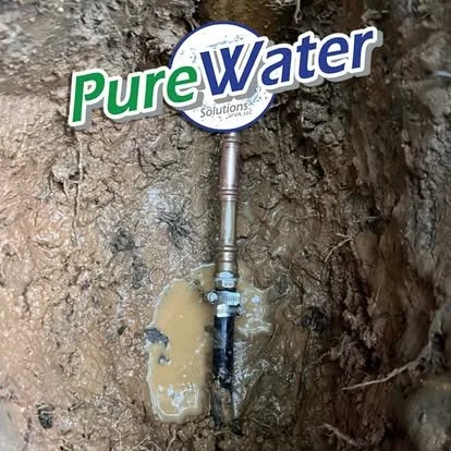 A water utility tap labeled 'Pure Water Solutions' installed in the ground with muddy water leaking around it.