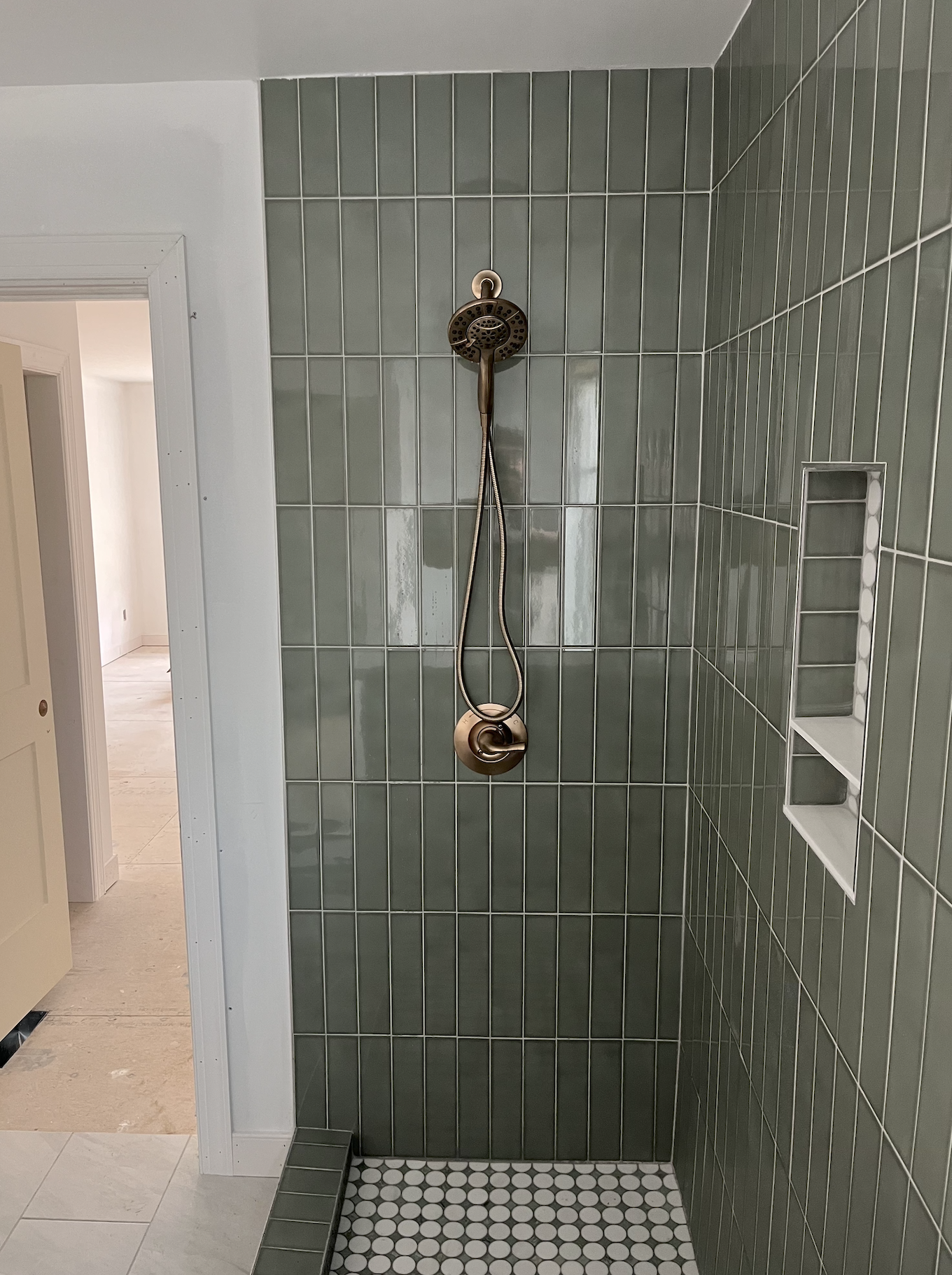 Green-tiled shower with a bronze showerhead and a built-in shower niche.