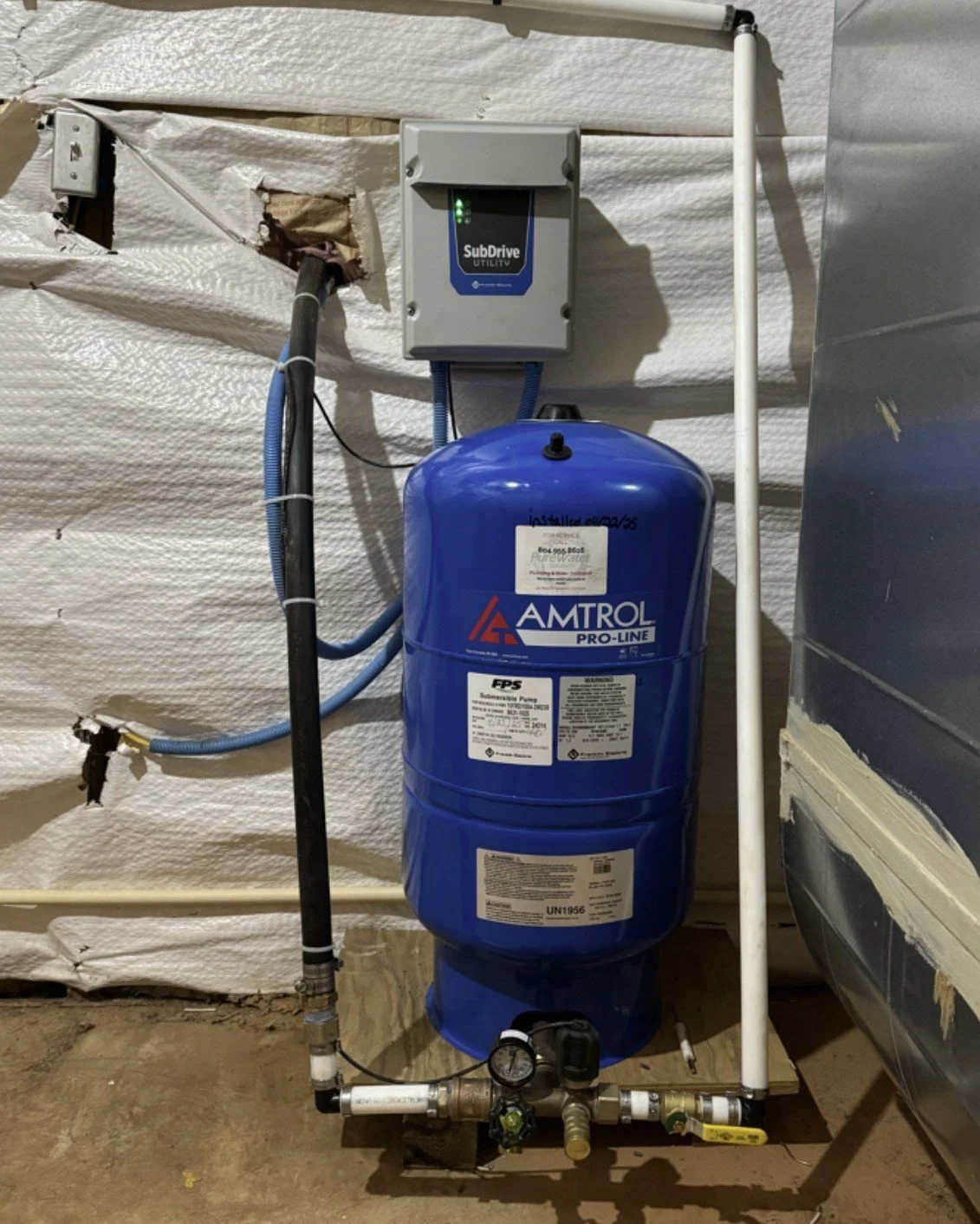 A water softener system with a blue tank labeled 'Amtrol Pro-Line' connected to pipes and a control panel mounted on a wall with white insulation material.
