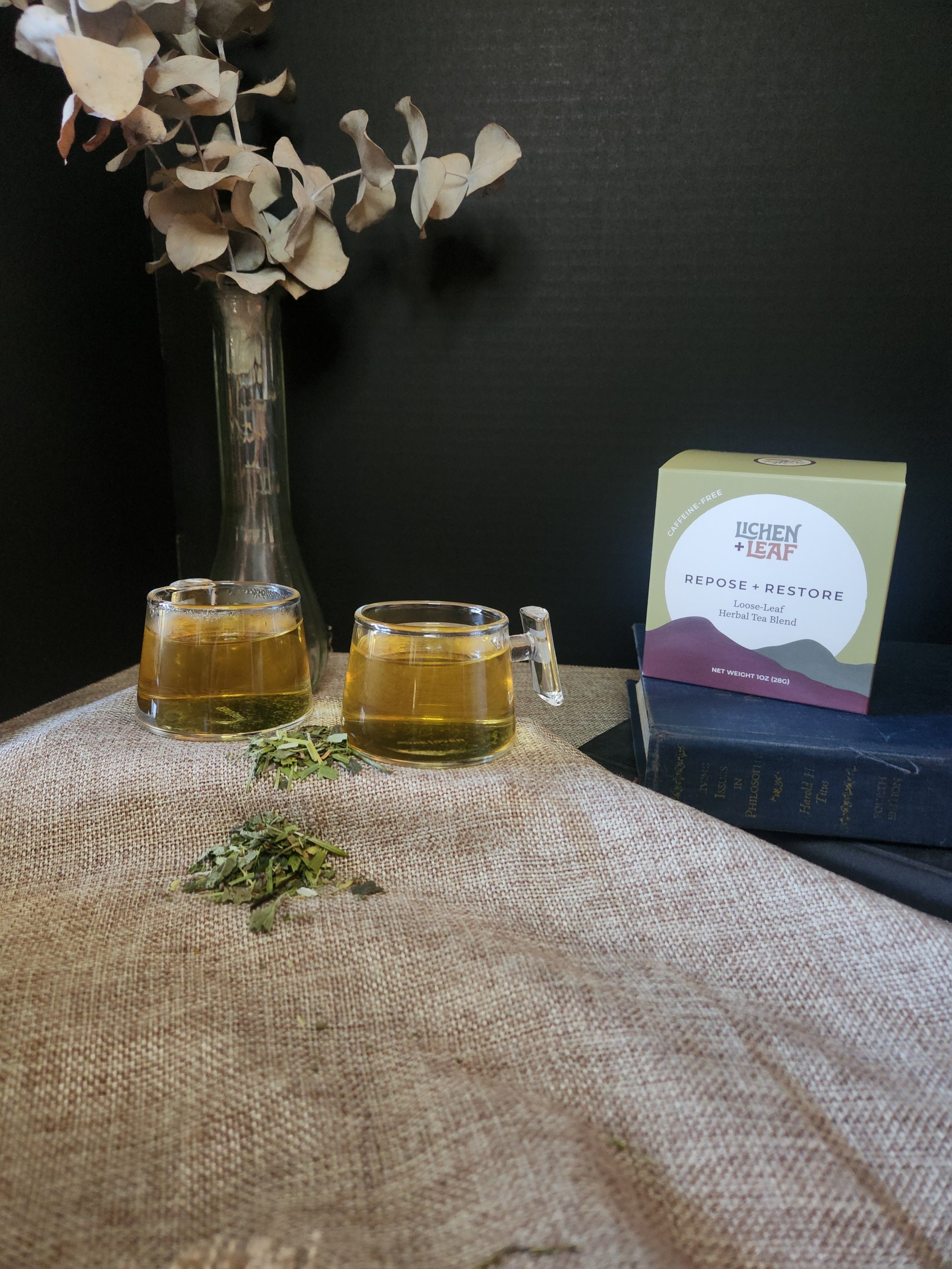 Two glass mugs of herbal tea with some dried flowers, and a box of Repose + Restore