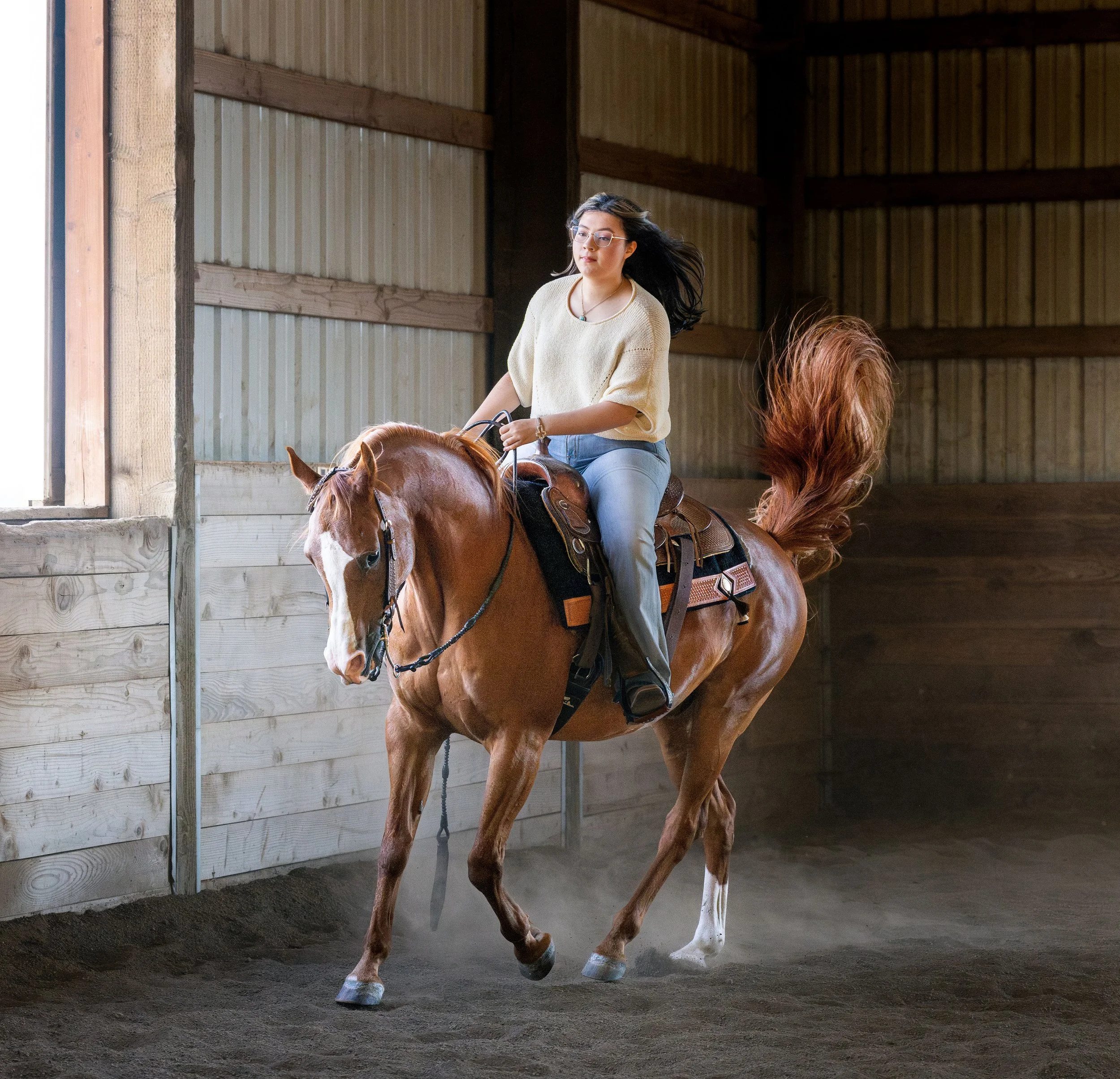 A woman riding a brown horse inside a wooden riding arena.