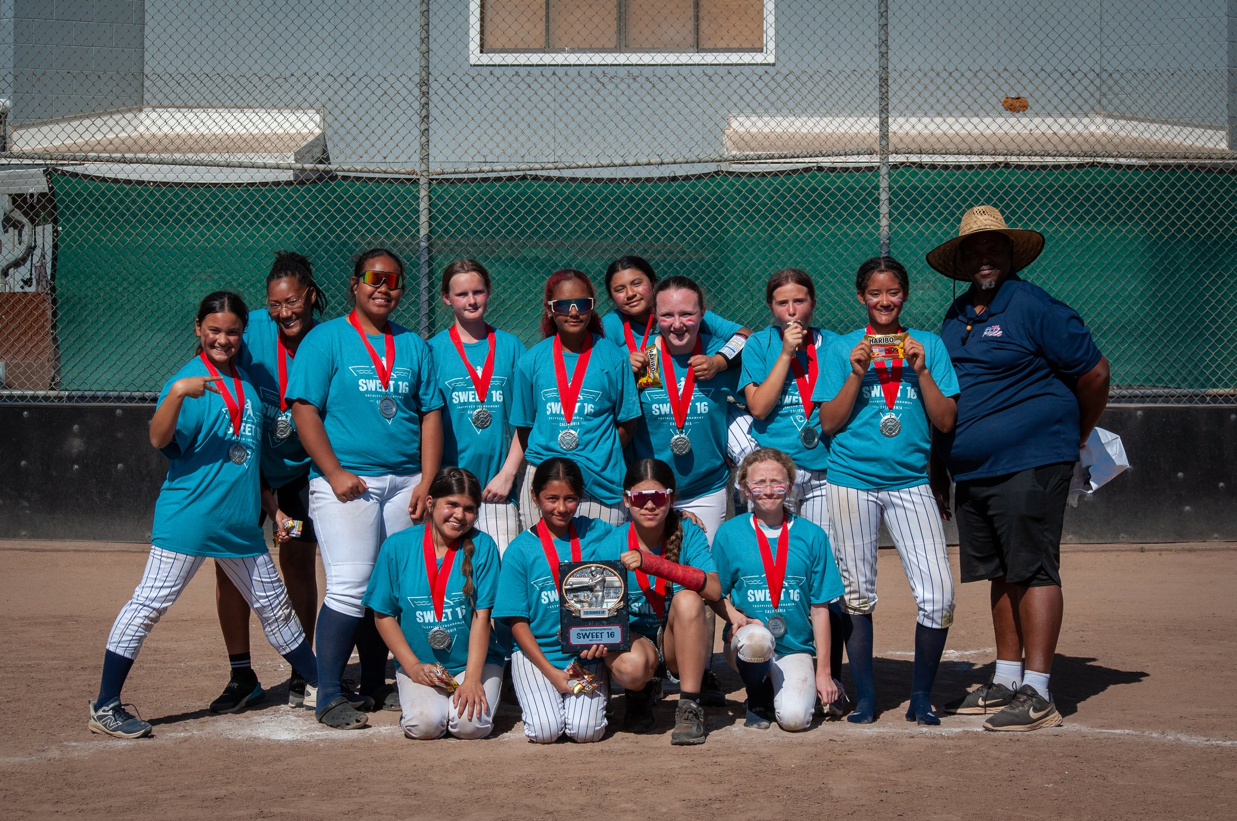 Youth baseball team and coaches posing with medals on the field, some kids wearing face paint, smiling after a game or tournament.