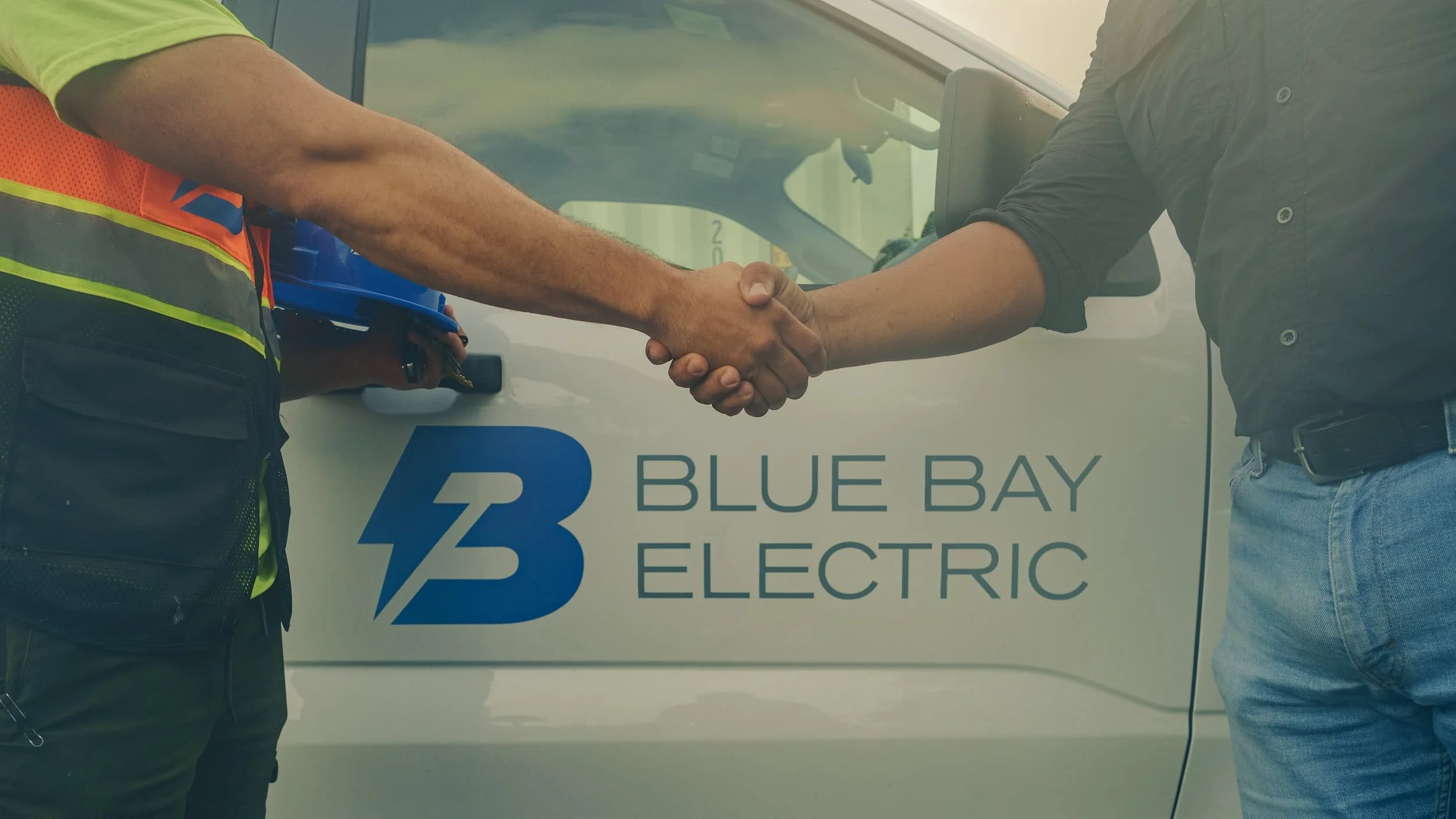 Two men shake hands in front of a White van with the logo and text 'Blue Bay Electric' on its side. Cinematic Editorial Pictures in Tampa Florida. Small brand business on tampa florida